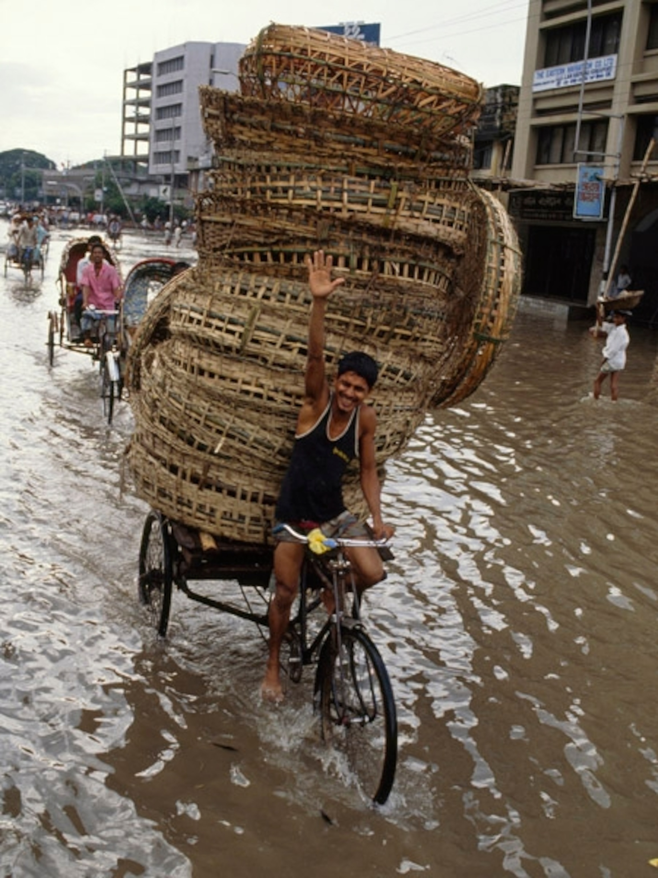 Man on a bike pulling a tower of poultry baskets in a flood