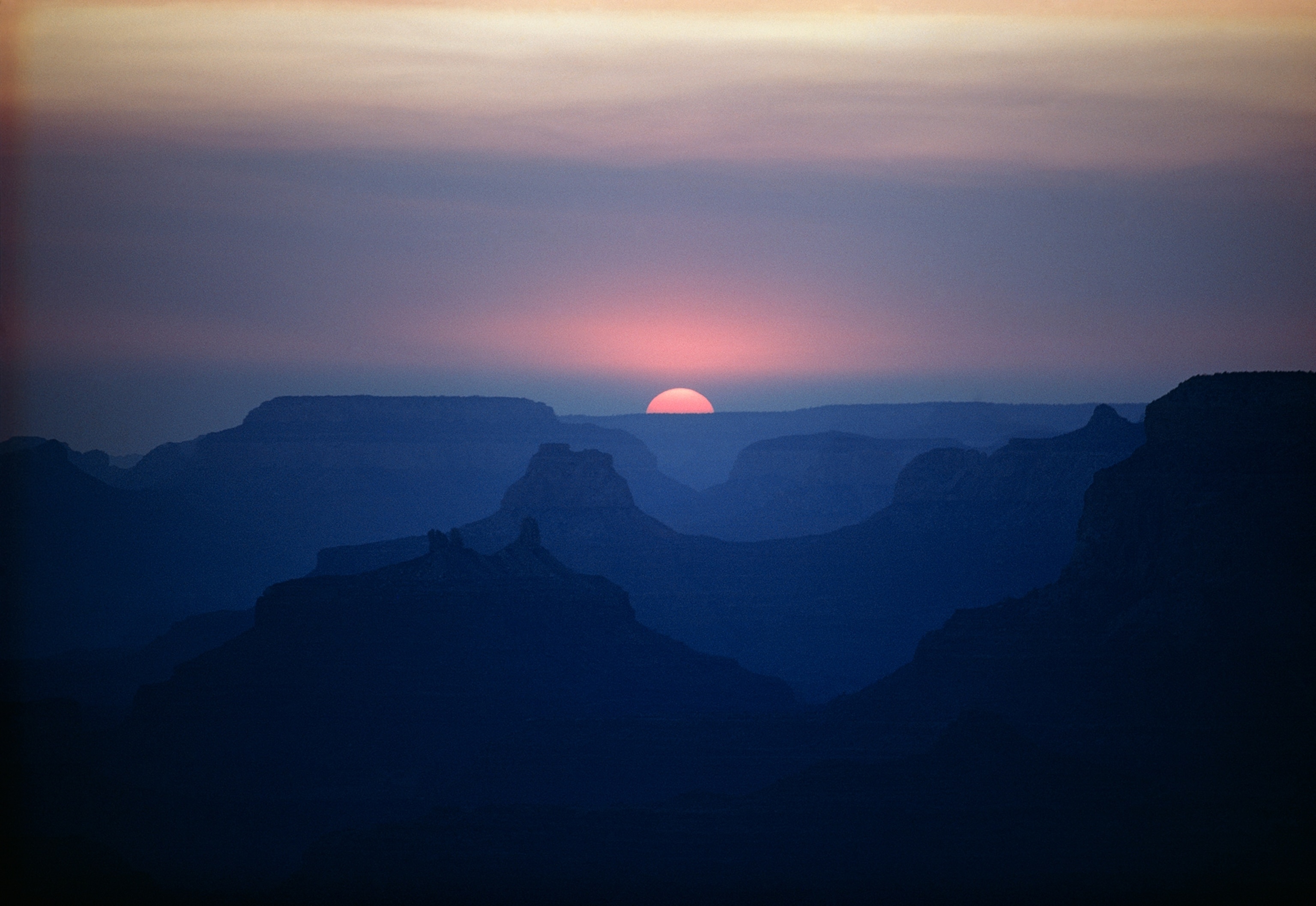 Sunset outlines ghostly silhouettes of canyons beyond Lipan Point.