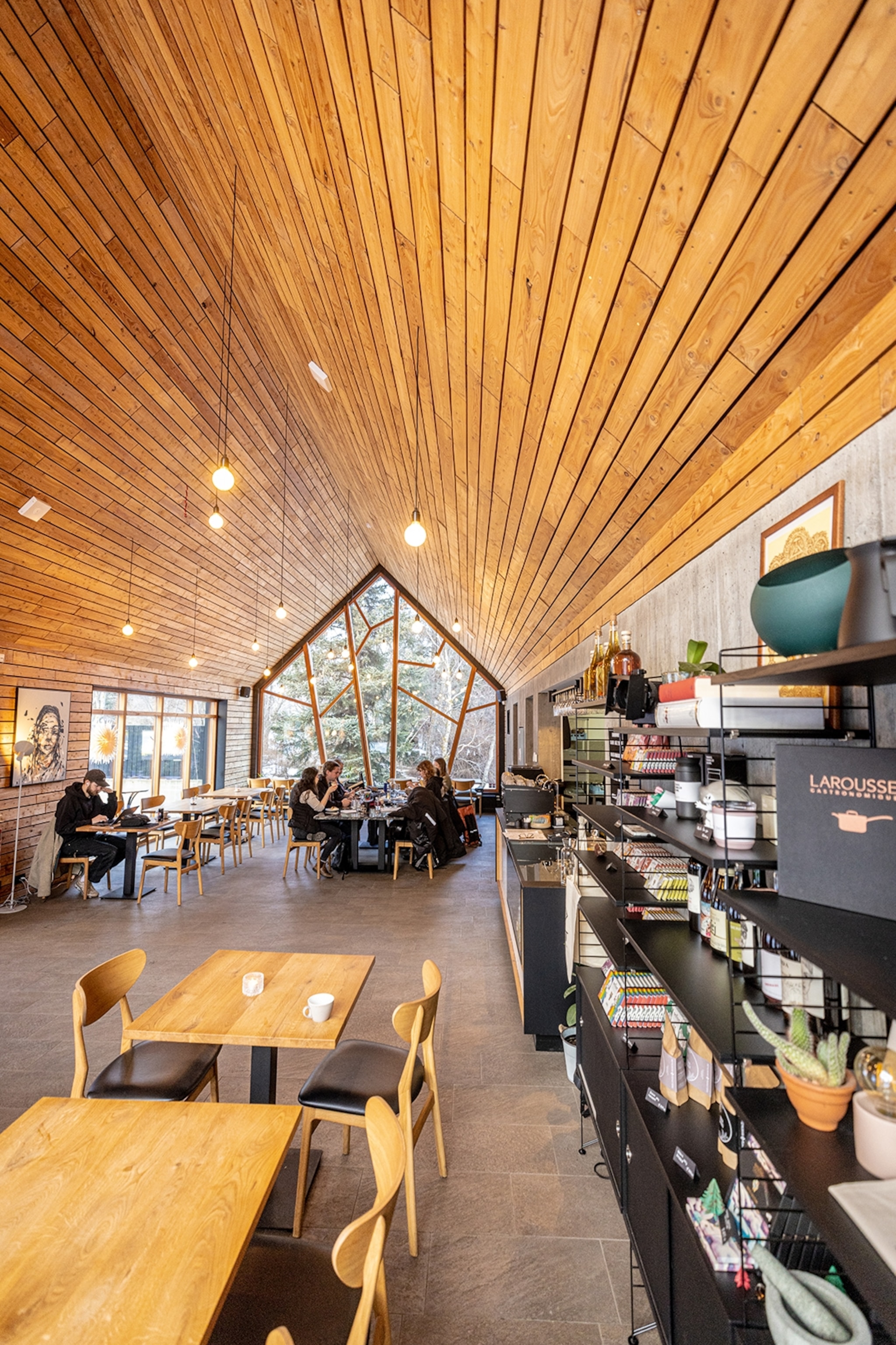 The interiors of a long cafe with a five-corner window showing the trees and bushes of a botanical garden.