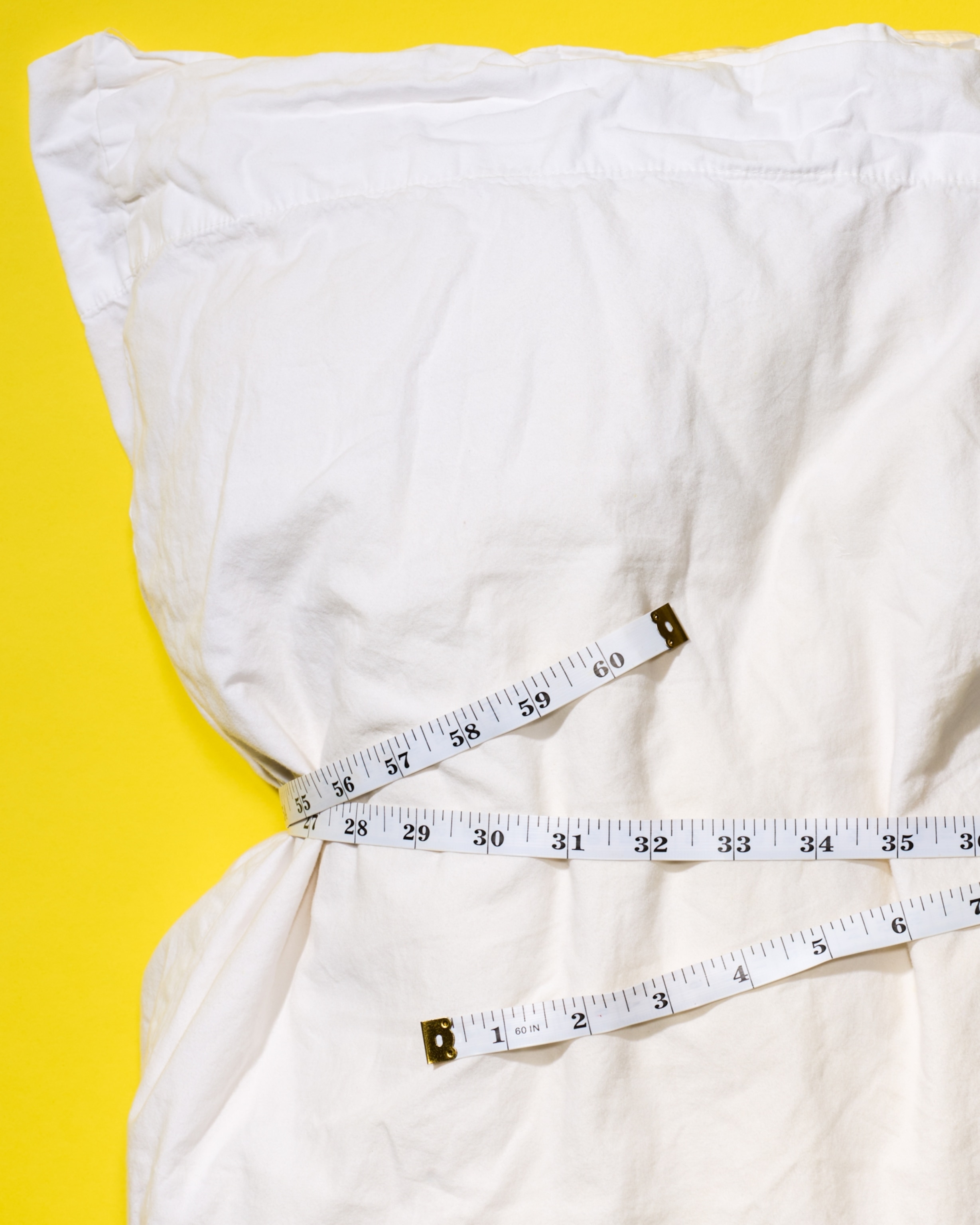 A pillow cinched by a tape measure on a yellow background.