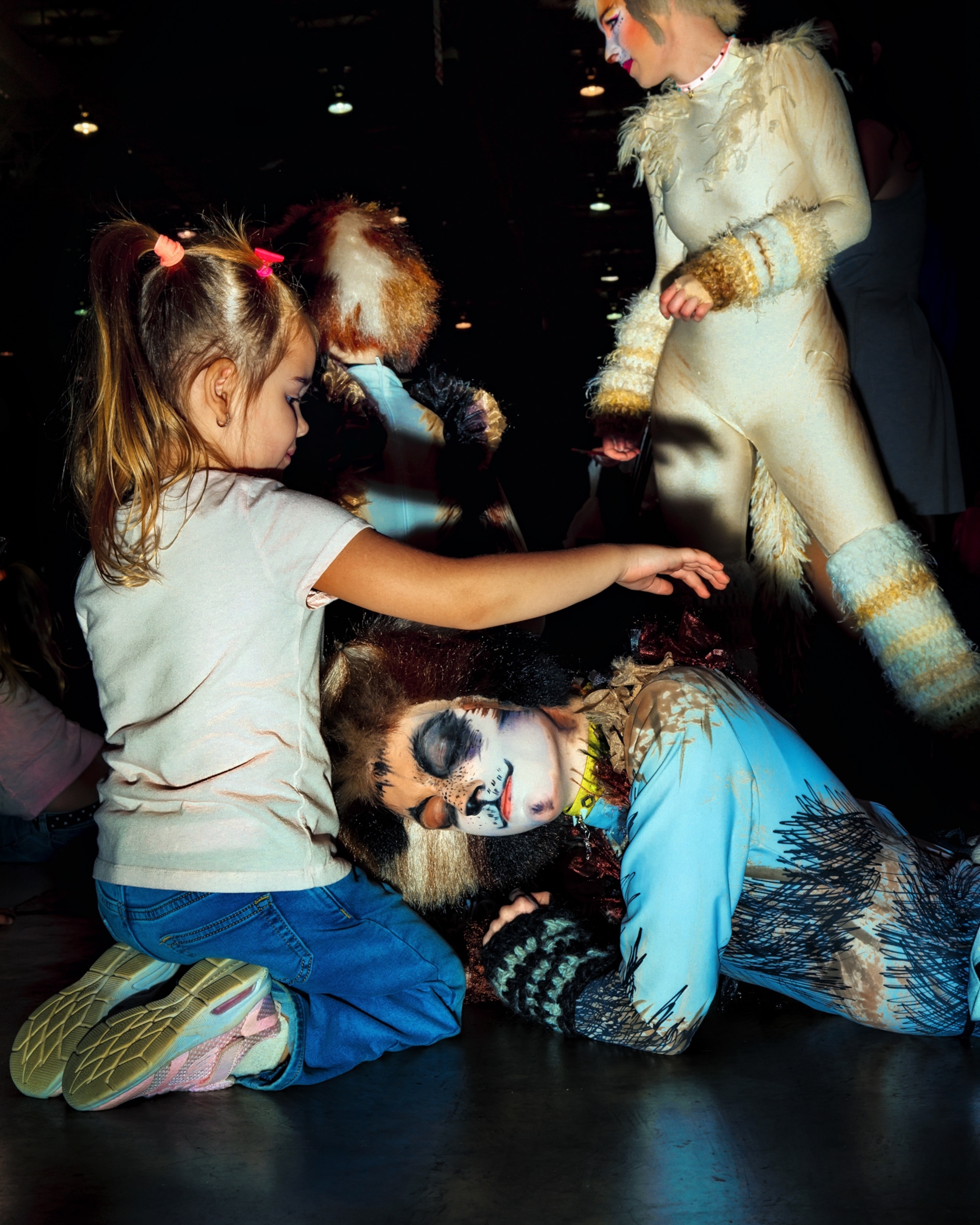 A performer dressed as a cat from the musical Cats, playfully resting her head in the lap of a young girl