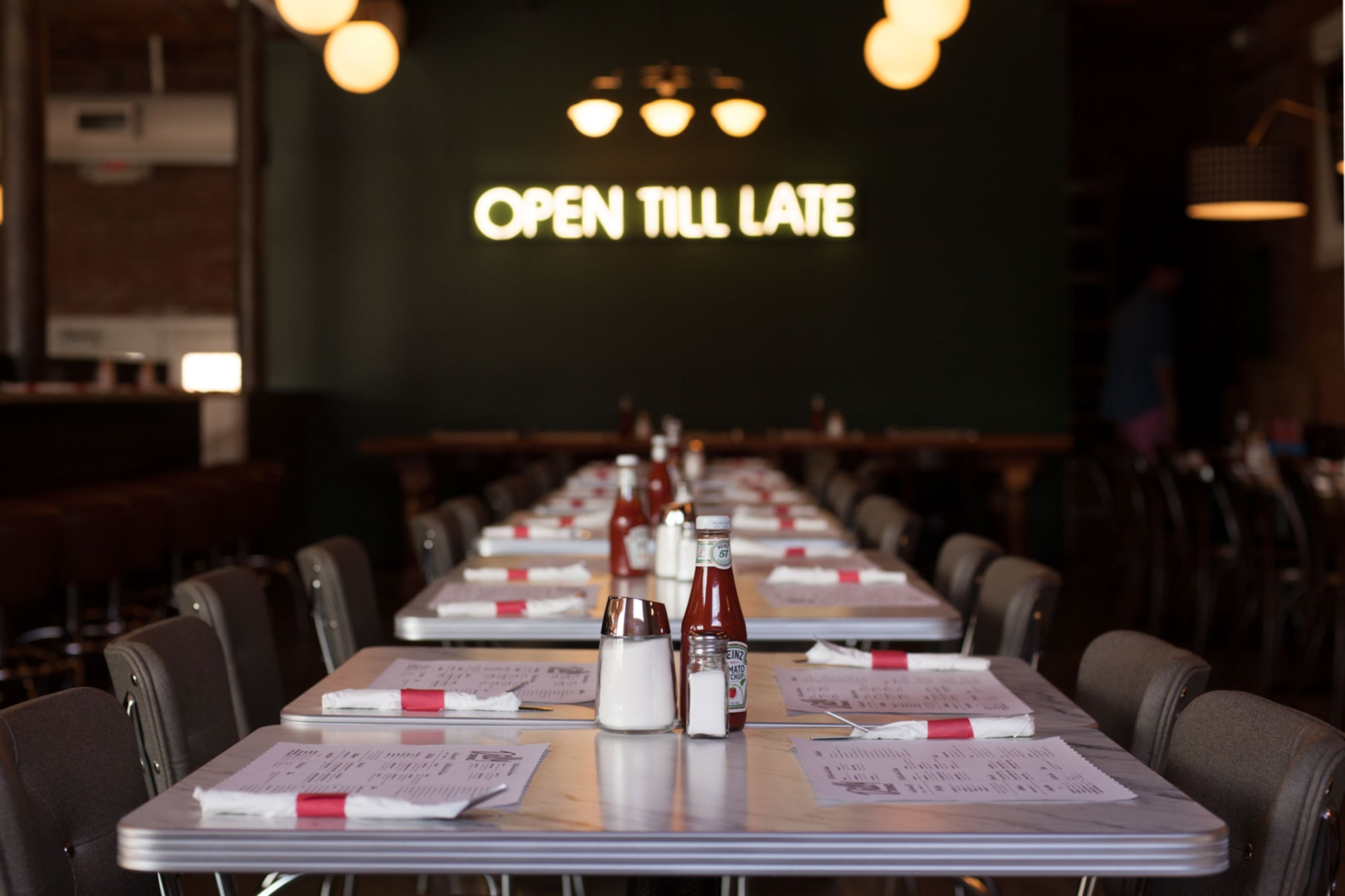 An eye-level view of a diner with tables and a neon sign saying 'open til late'.