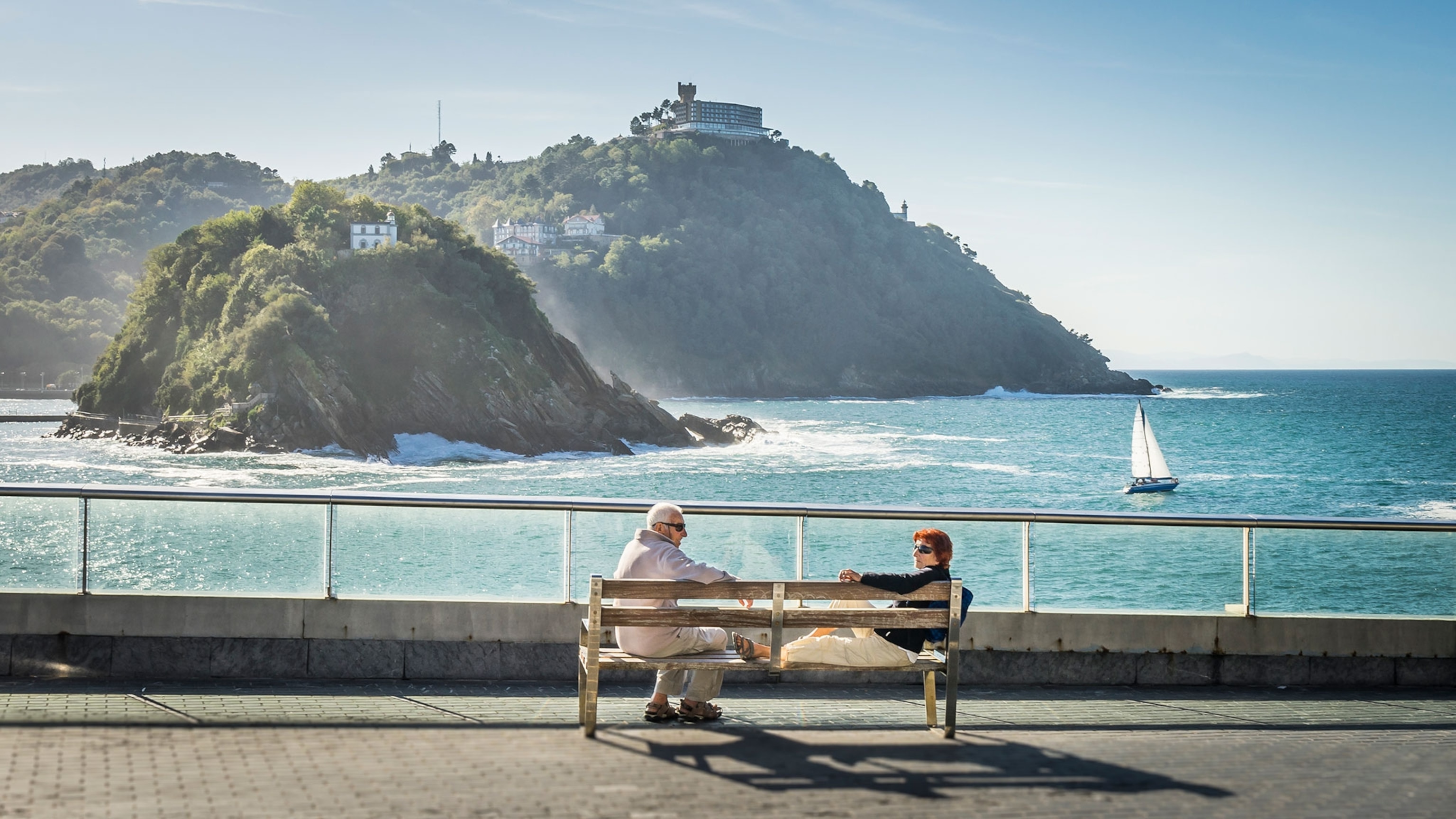 two people sitting on the bench by the ocean