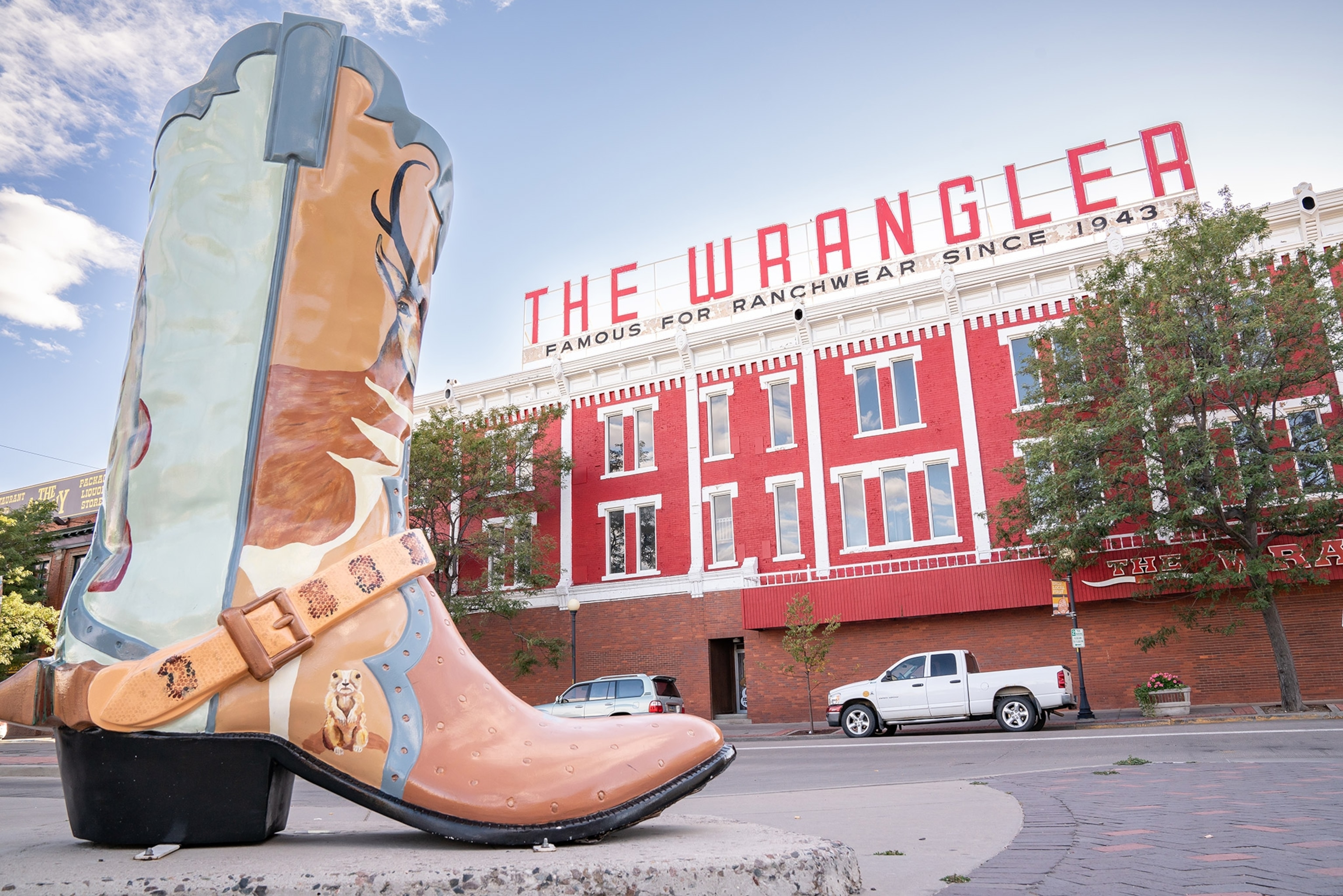 An oversized statue of a cowboy boot, painted decoratively, in the foreground, with a large red building with "THE WRANGLER" sign behind.