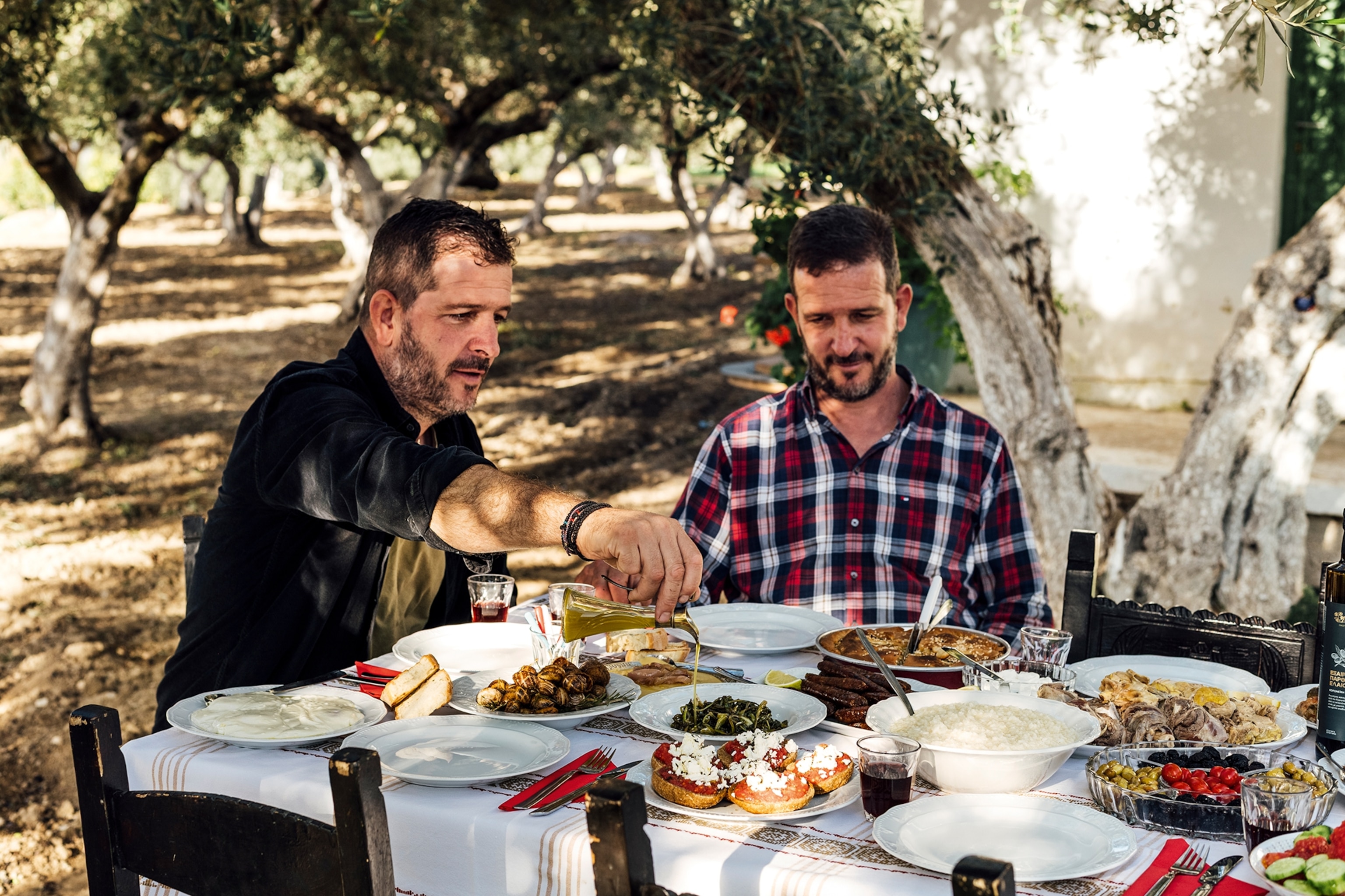 Two men share a mezze spread at an outdoor table at a farm.