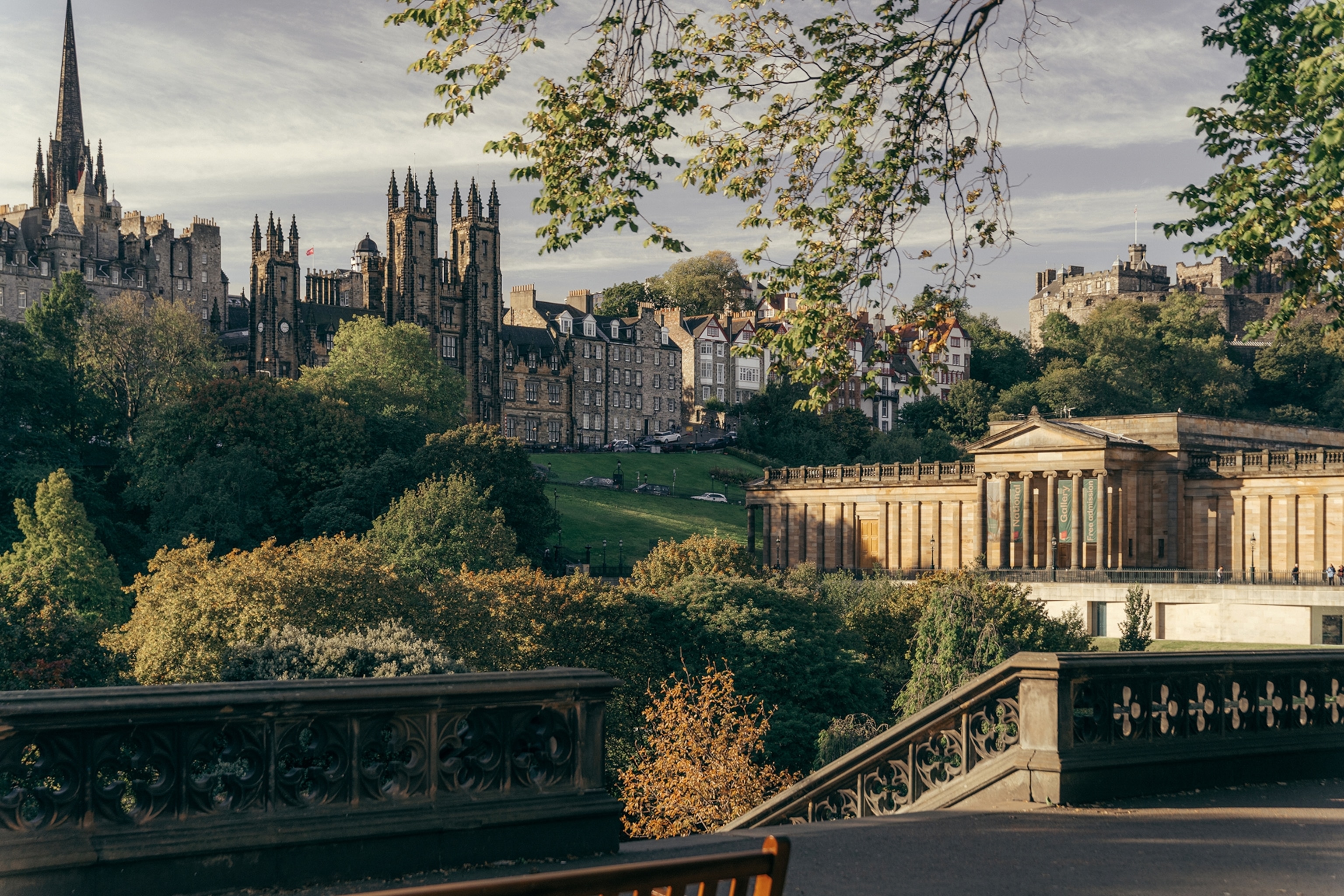 A scenic, urban view of a hill park with a stone-columned building and residential houses lining the horizon.