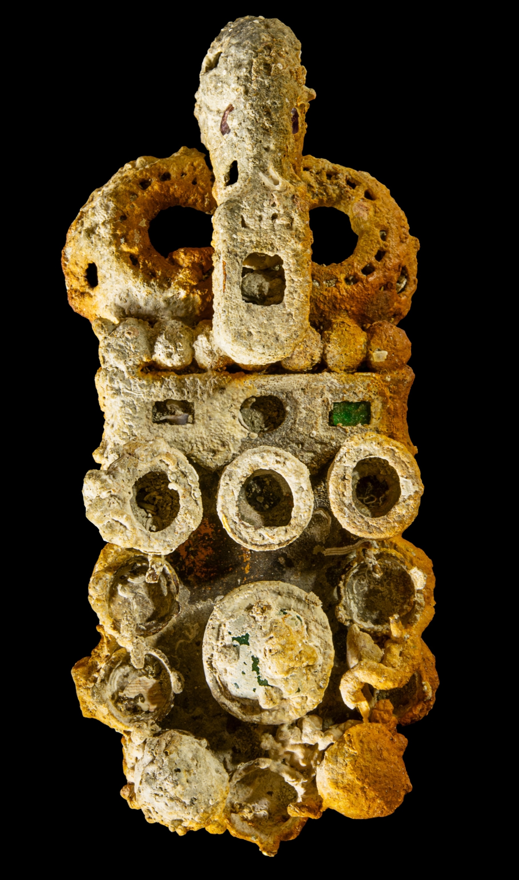 An artifact with various green, purple, and red gem stones. The gemstones are not visible under a build up of brown dirt