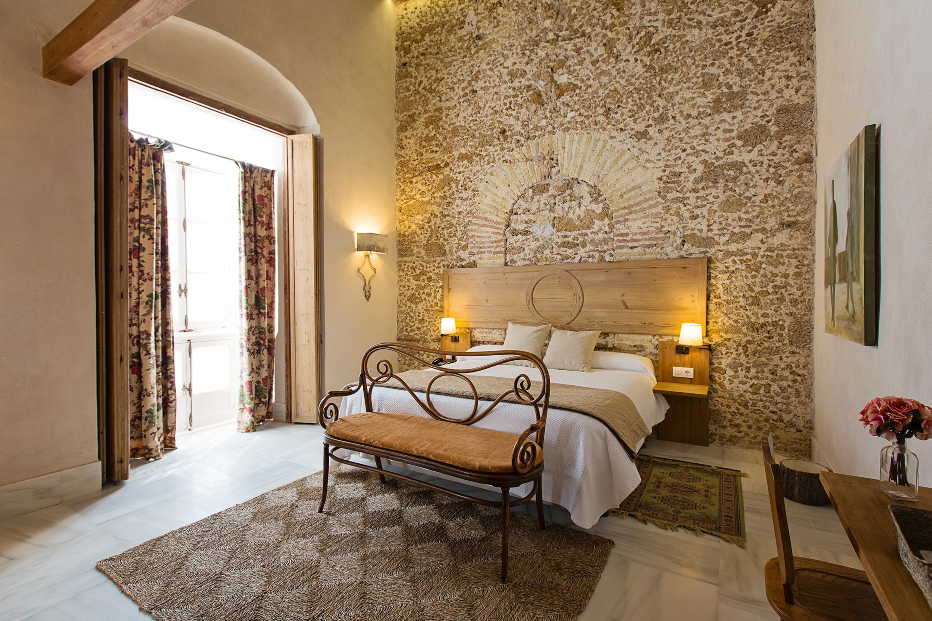 The spacious interiors of a traditional hotel bedroom with an original stone brick wall and queen size bed.