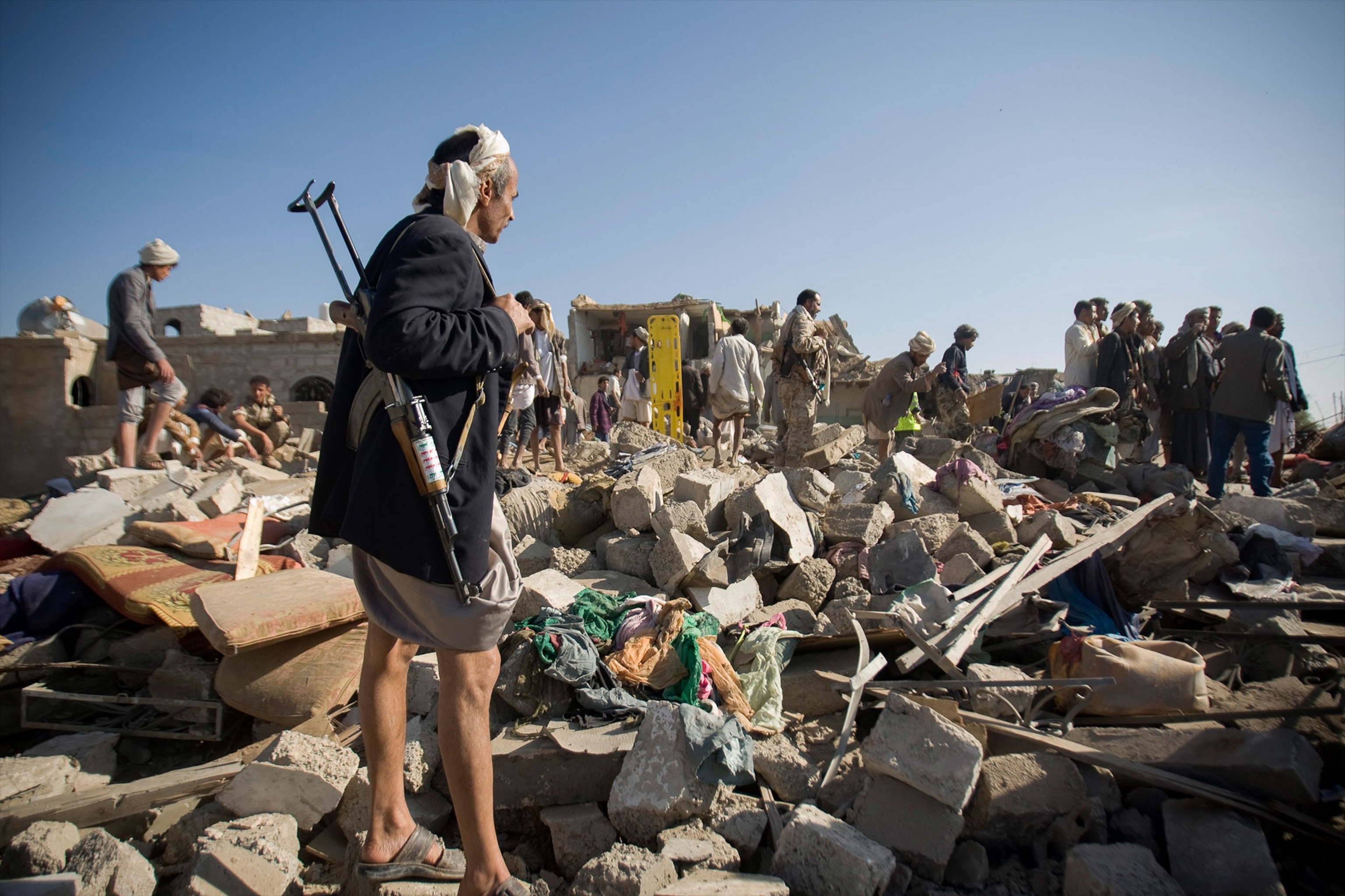 a Houthi Shiite fighter standing guard as people search for survivors in Yemen