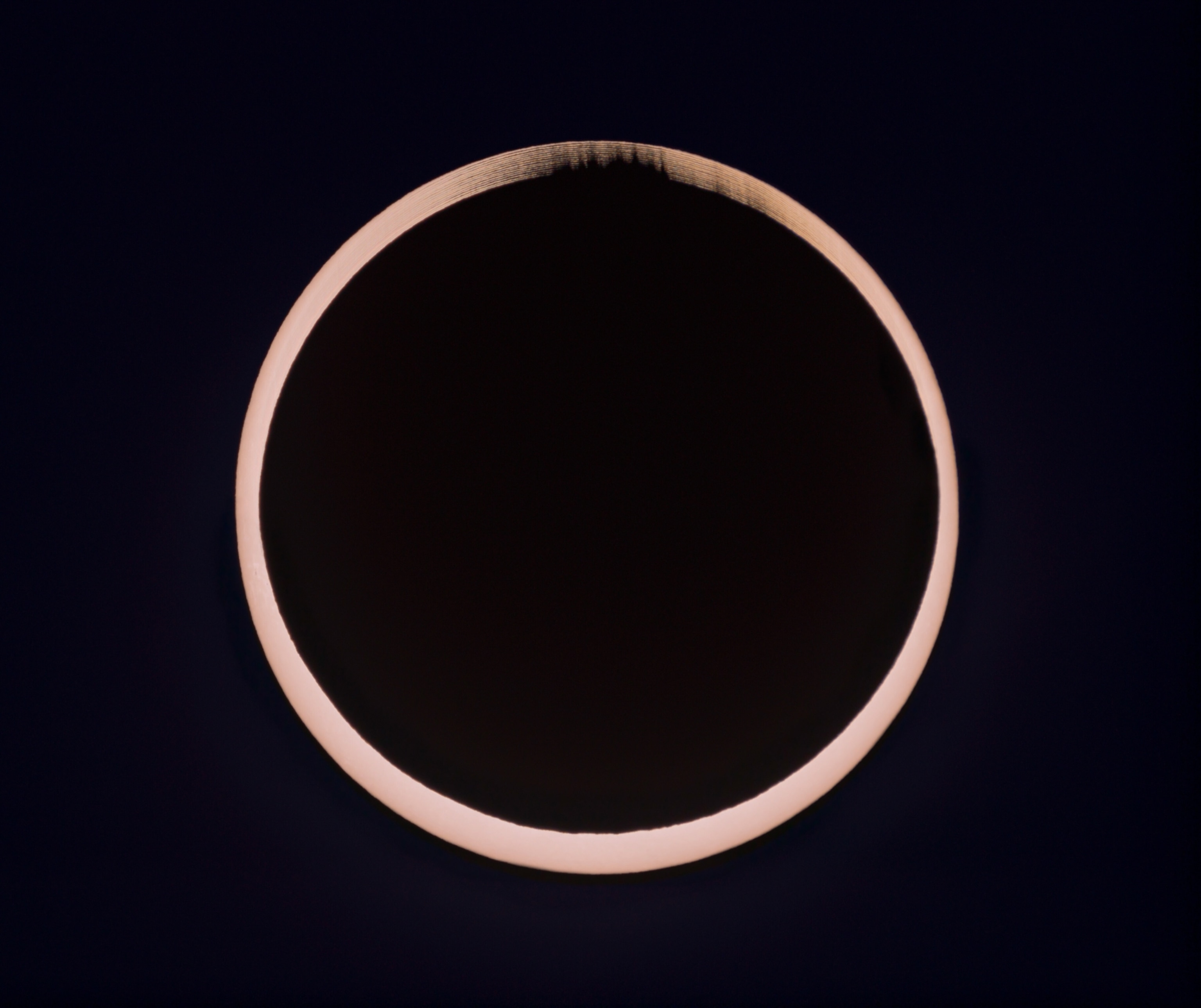 A glowing ring of sunlight surrounds a dark circle in the center, set against a deep blue background.