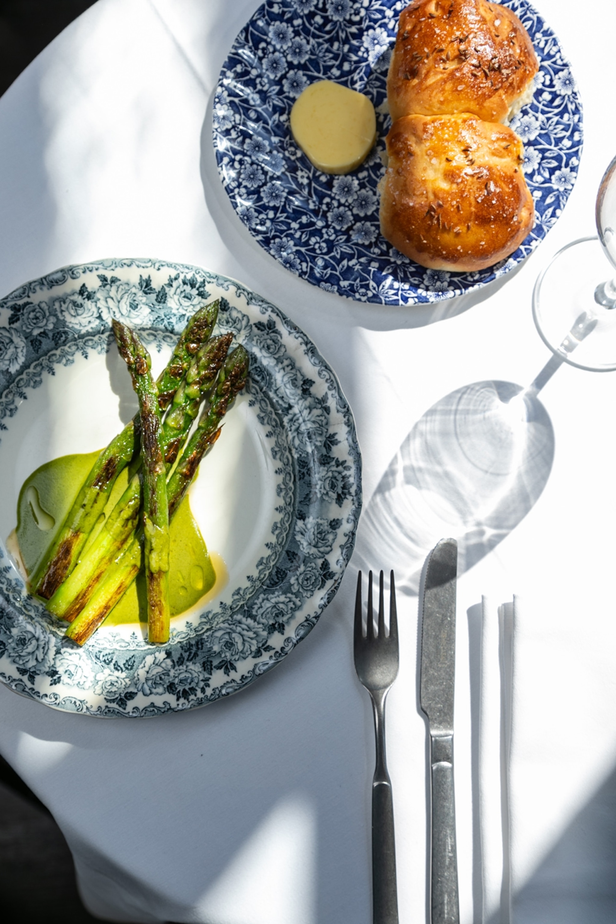 A plate of asparagus and milk bread buns on a set table with cutlery.