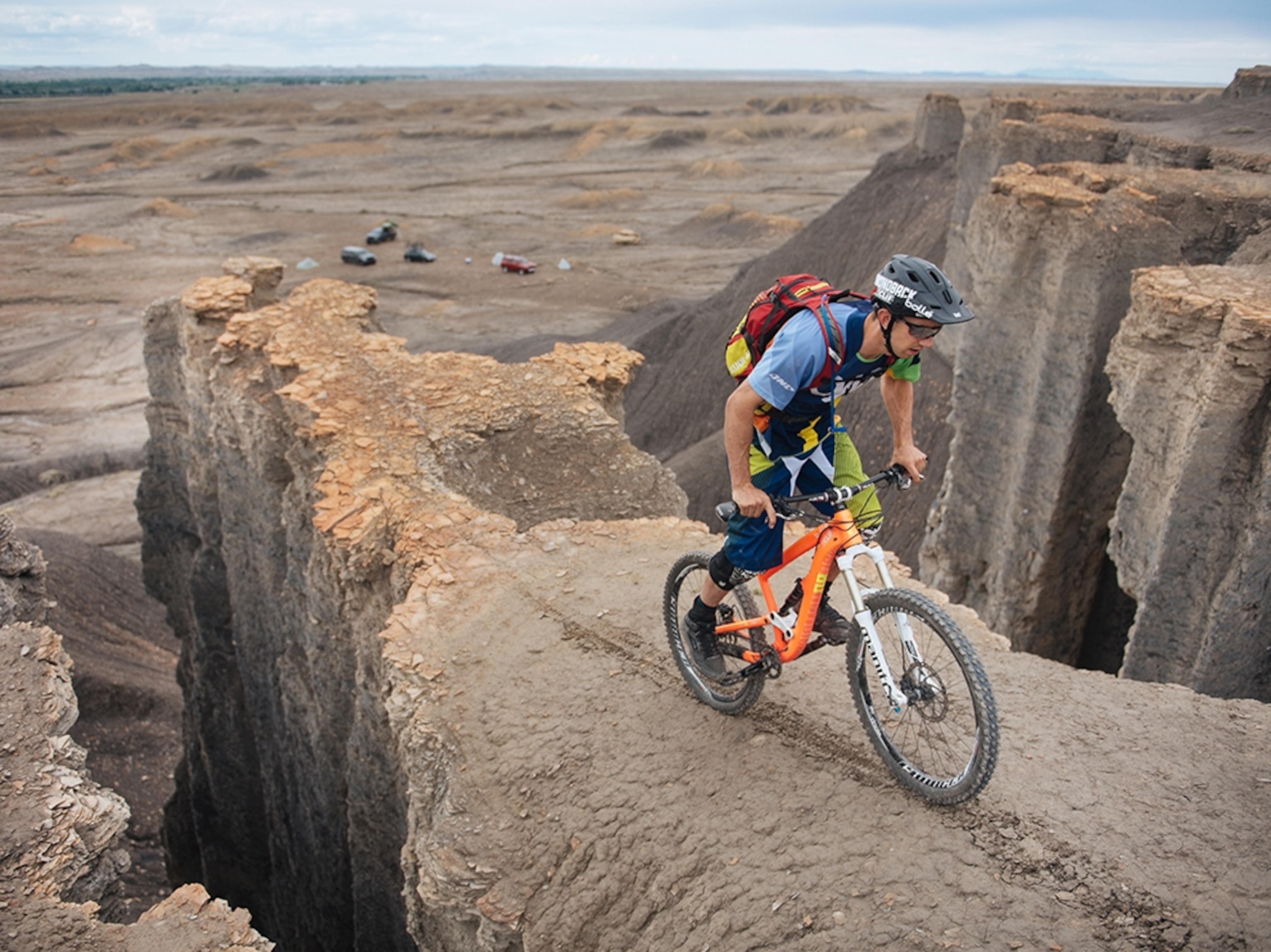 a mountain biker riding along the edge of a thin rock formation that drops off steeply.