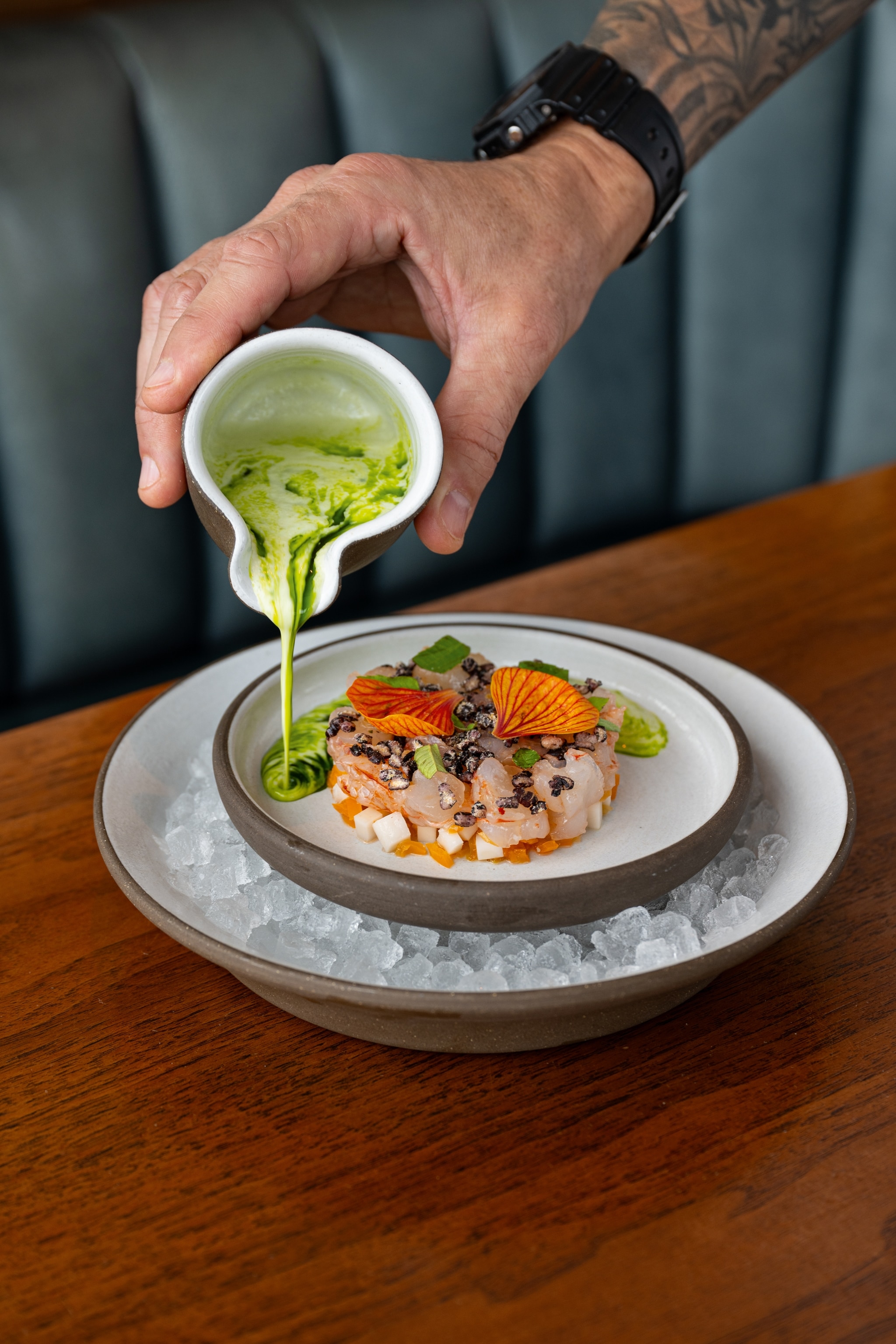 Person pours sauce onto luxury meal, which is laying on a bed of ice