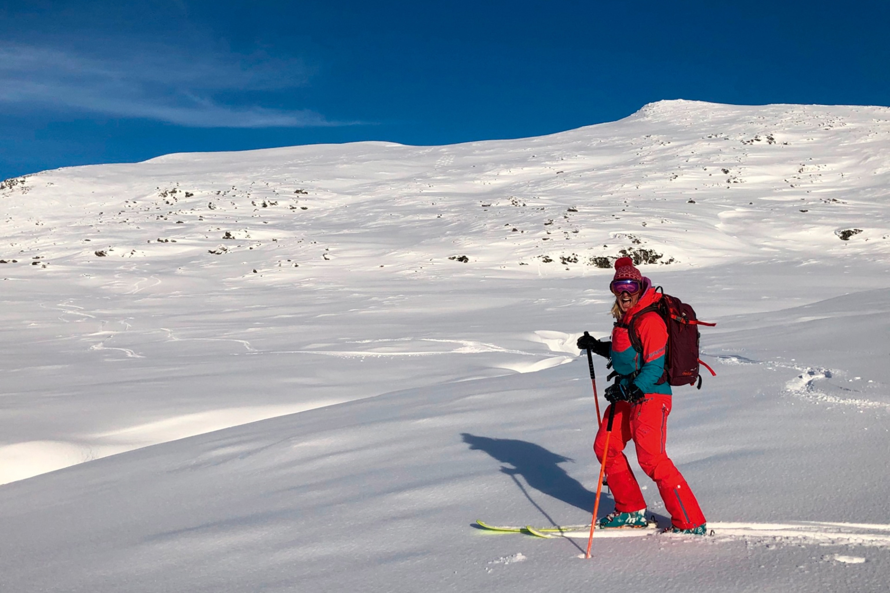 A smiling woman skiing across a flat yet snowy mountain plateau.