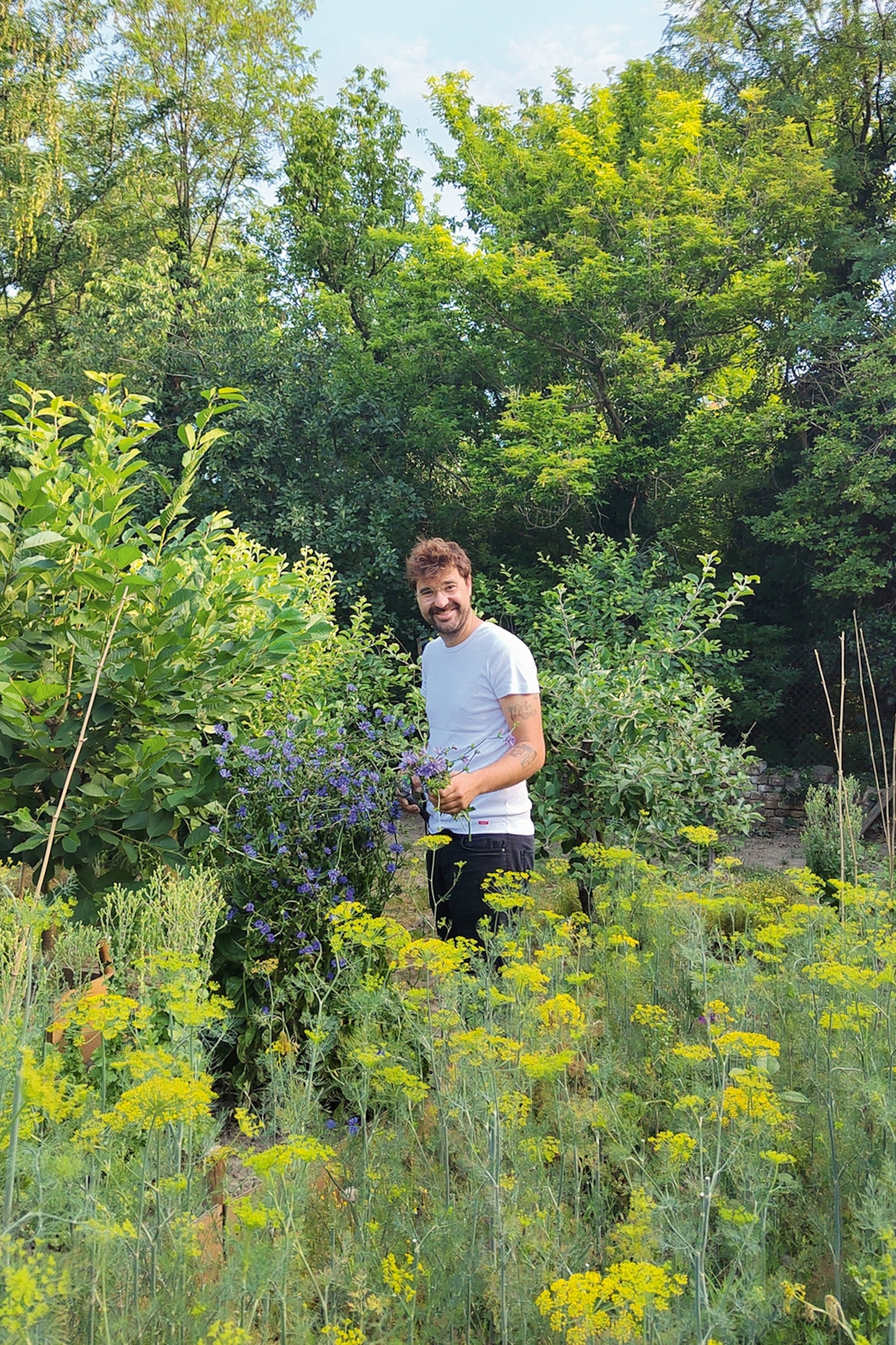 A smiling local surrounded by a lush kitchen garden and trees in the background.