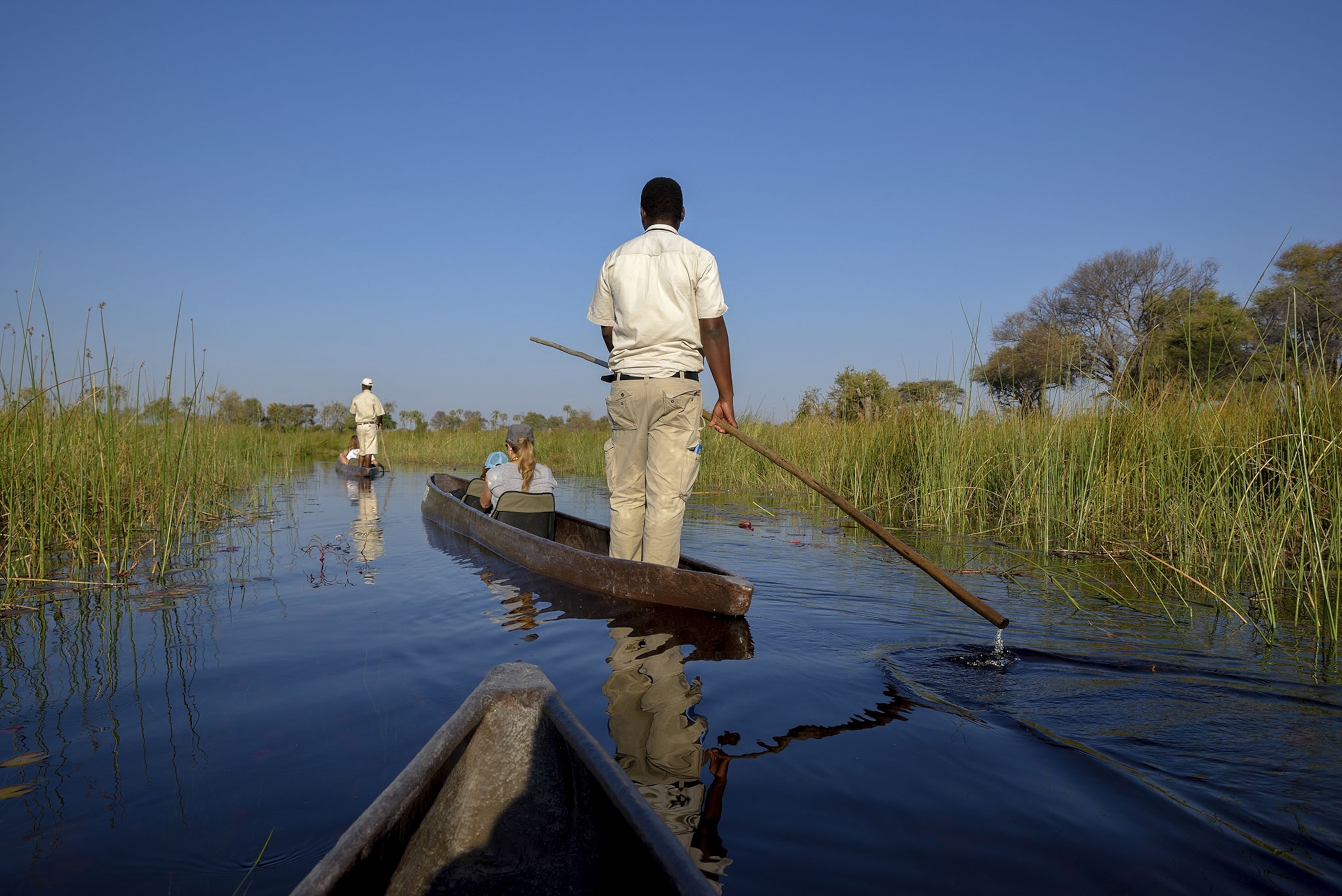 A man stands on a boat travelling down a river.