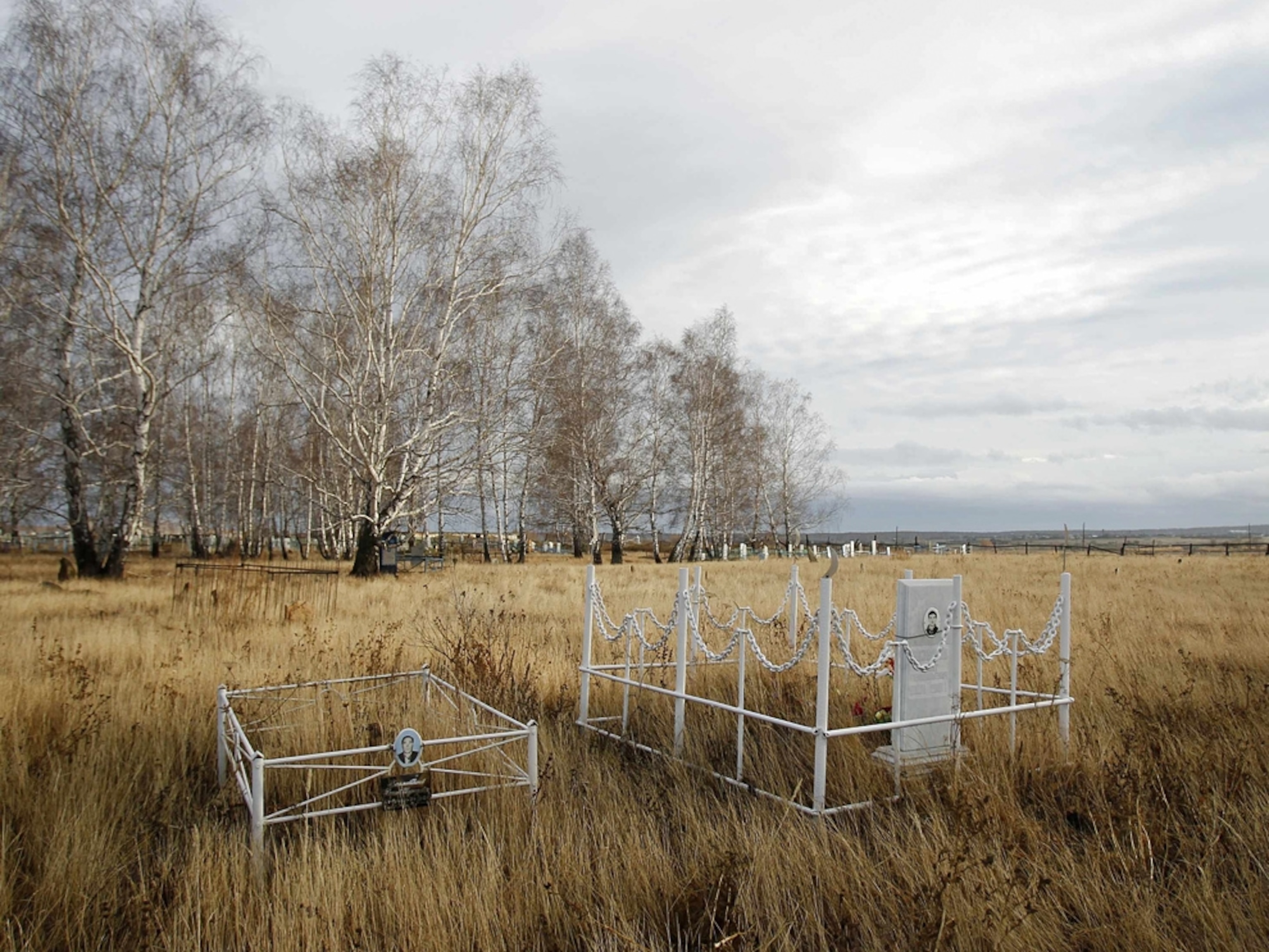 Two graves stand in a lonely, grassy field.