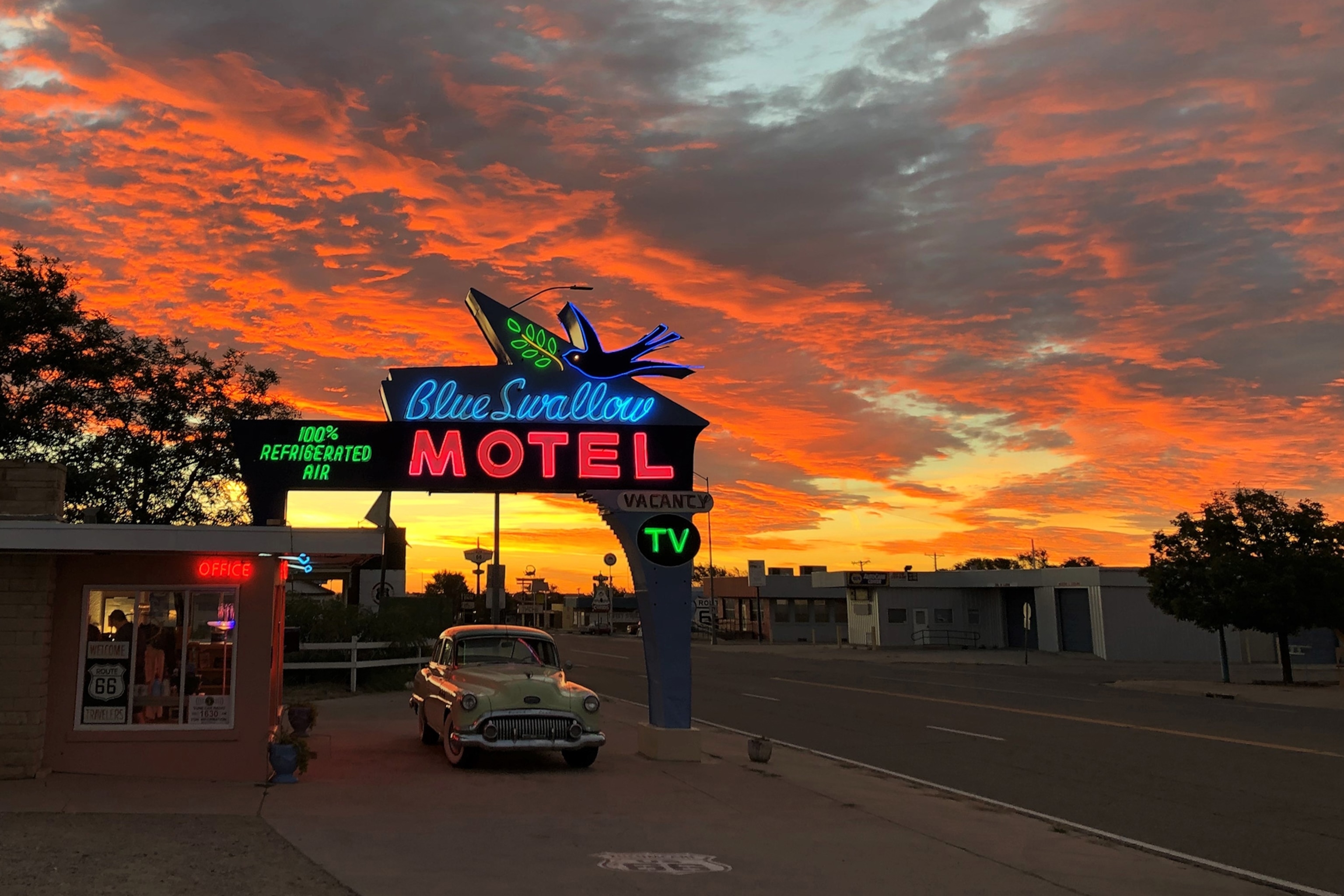 A driv-through hotel check-in station with an LED sign to the backdrop of a burning sunset sky.