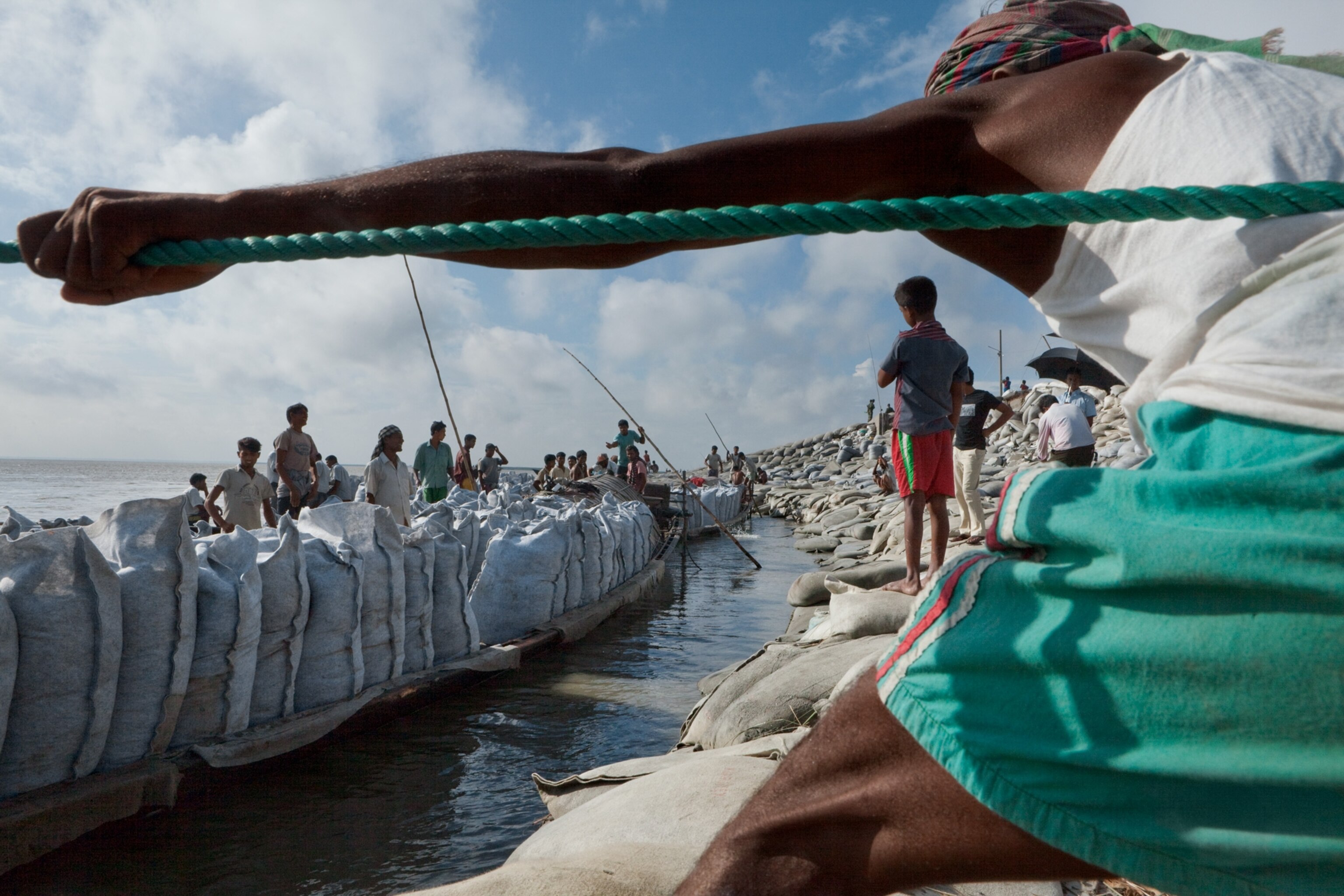 Bangladeshis in Sirajganj hauling boatloads of bagged sand to reinforce a levee