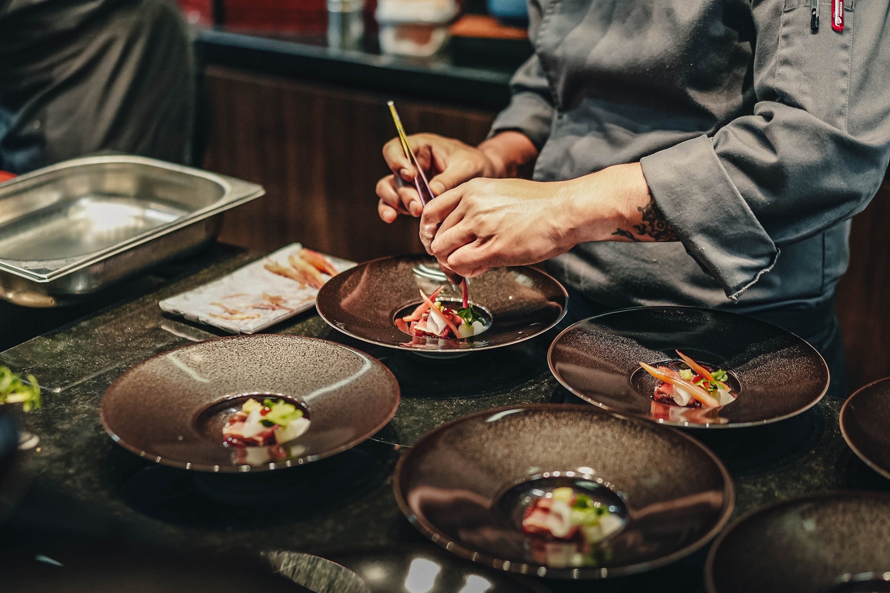 A chef adding the finishing touches to a finely arranged dish on a kitchen pass.