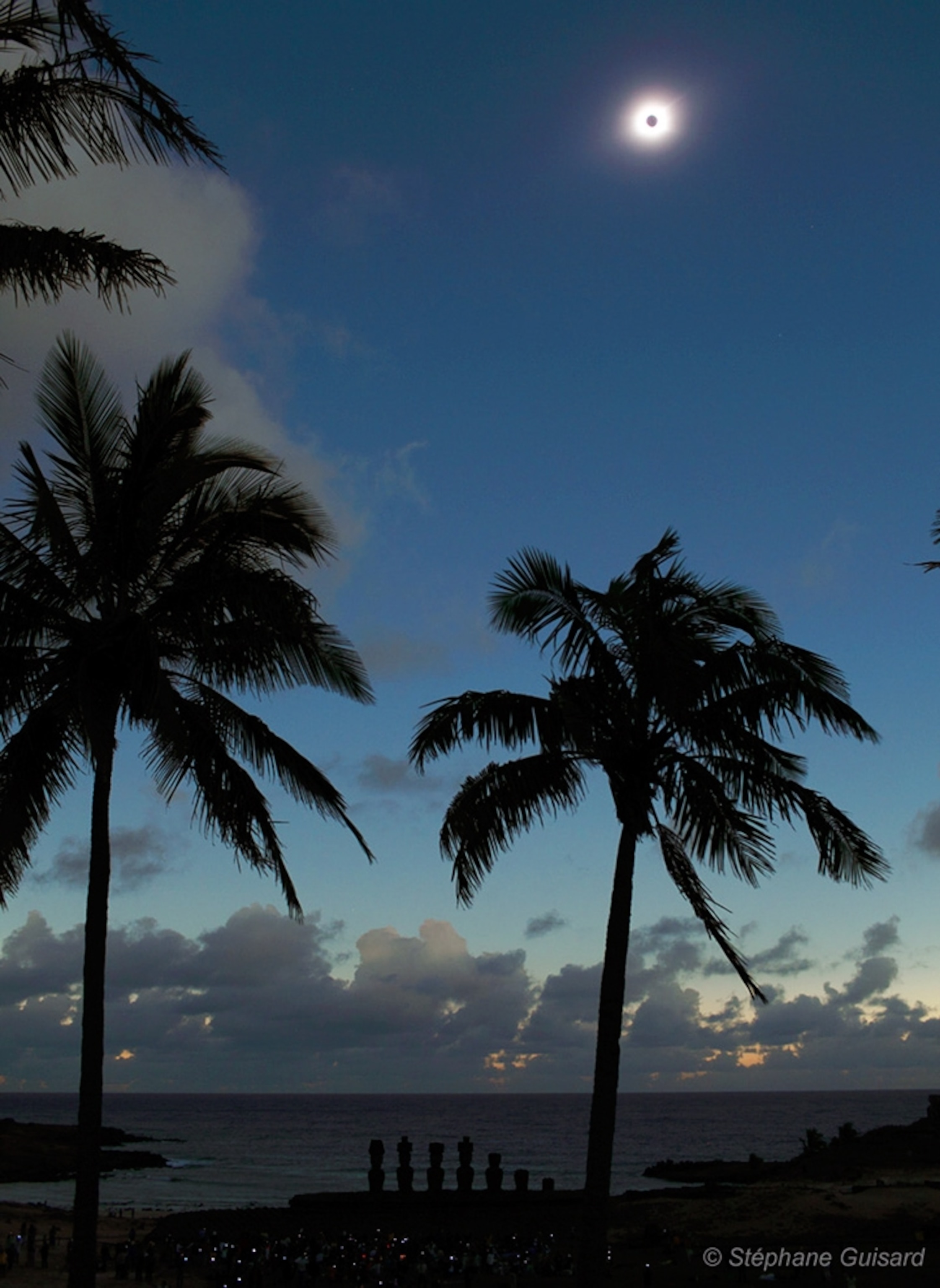 Picture of a total solar eclipse over Easter Island, with stone statues on the ground below.