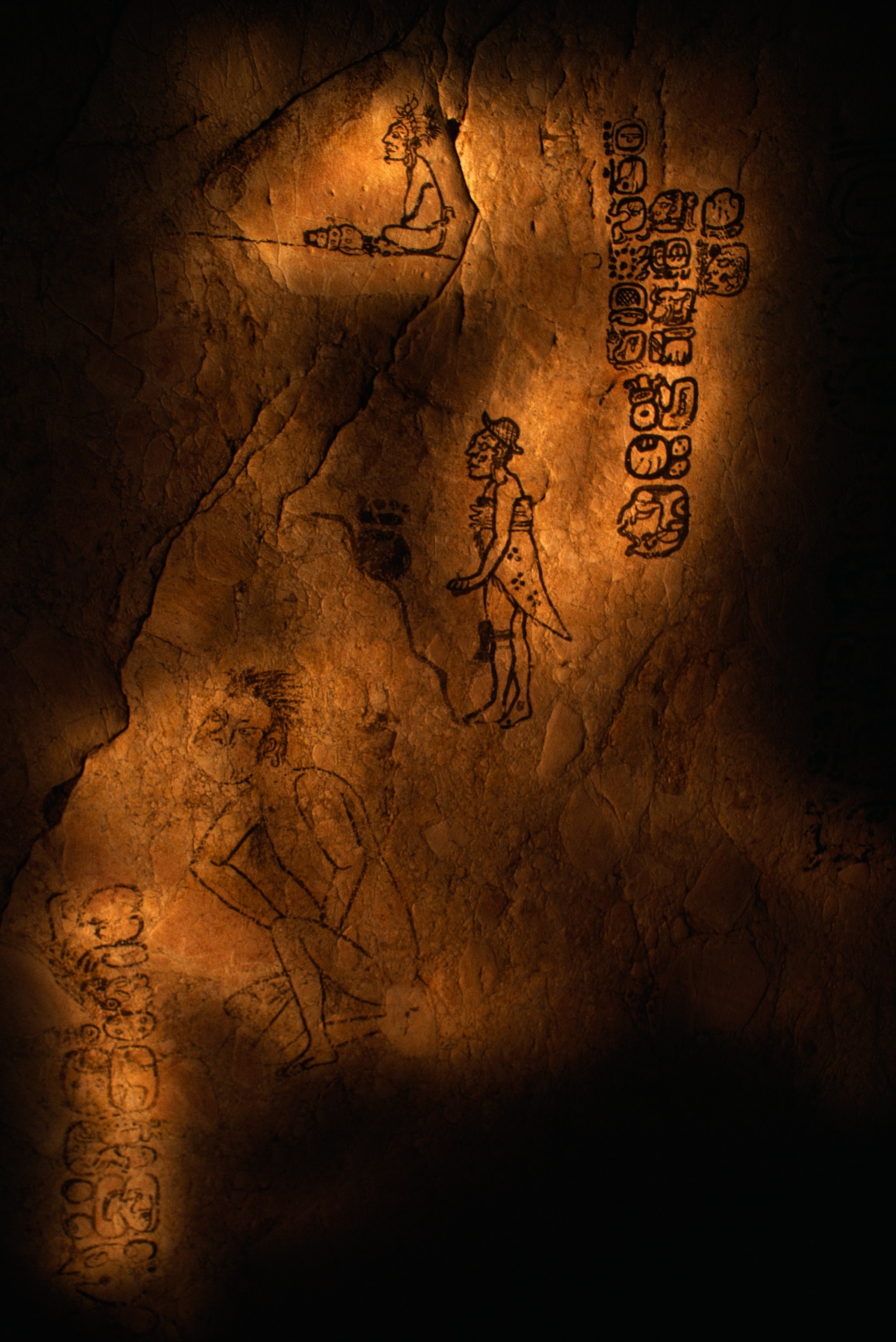 Ancient carvings on a dimly lit stone wall depicting human figures and hieroglyphs.