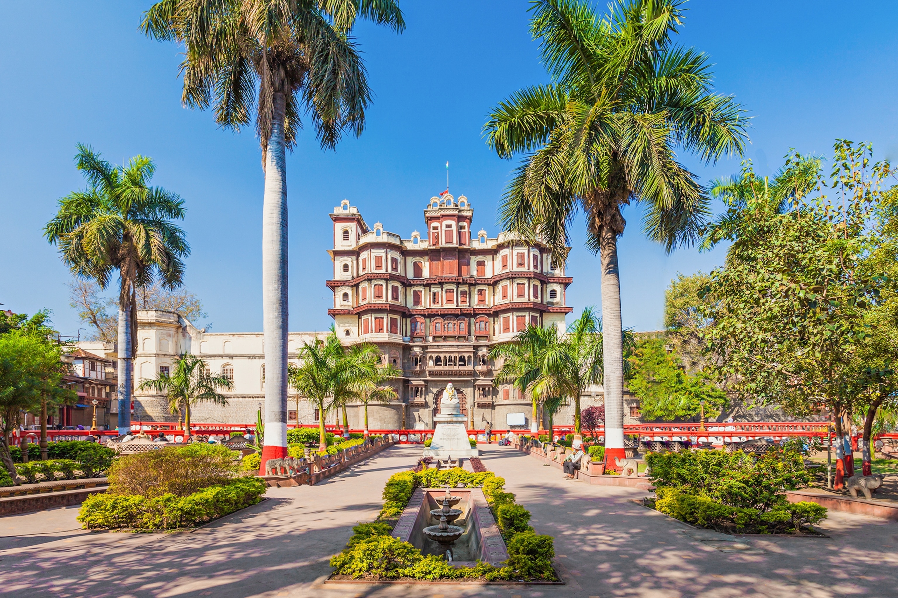 An Indian palace surrounded by palm trees with other city buildings in the background.