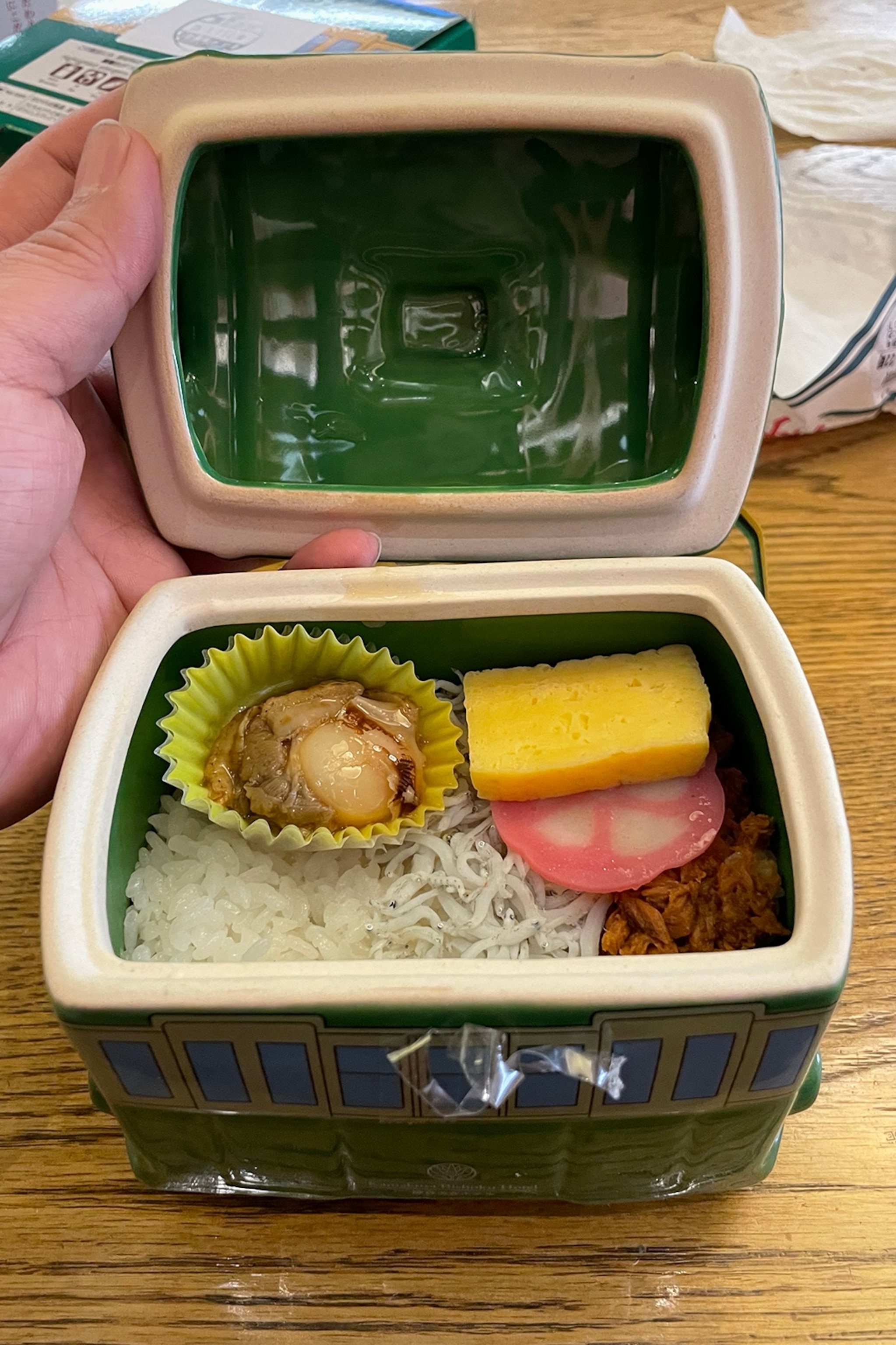 A ceramic bento box featuring clam, rice and vegetables.