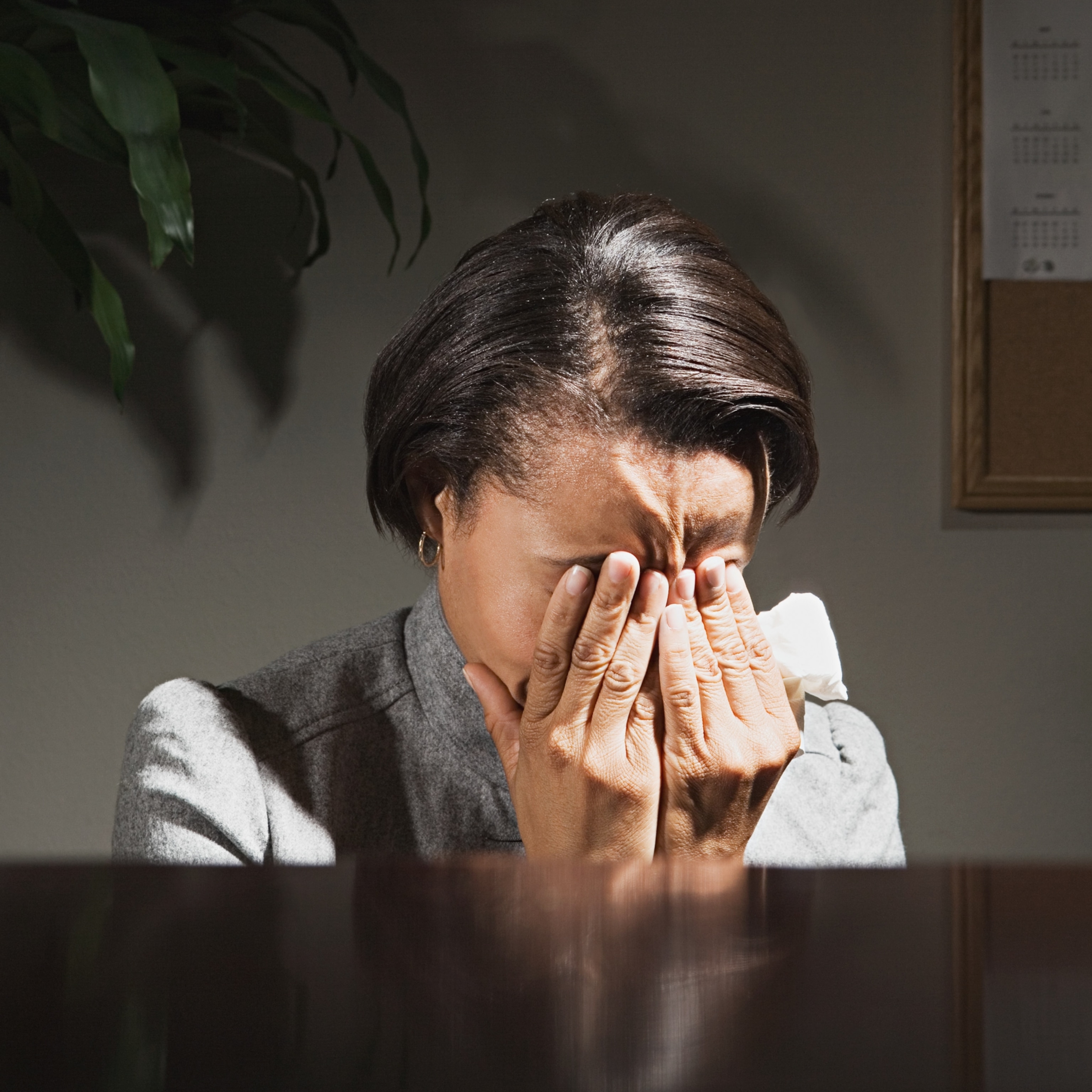 An office woman with her face buried in her hands as she suffers from a headache