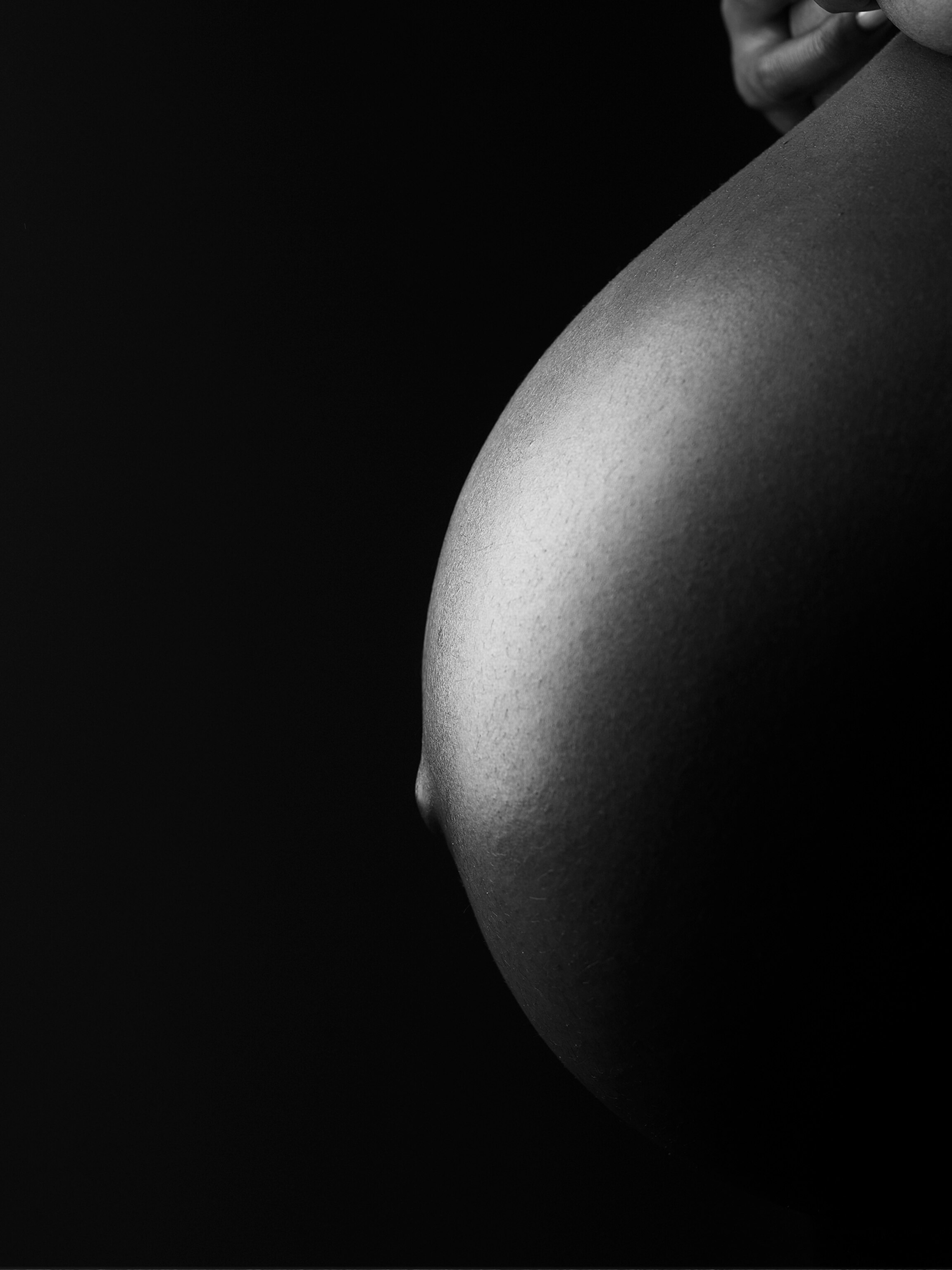 A profile view of a woman's belly while pregnant in black and white.