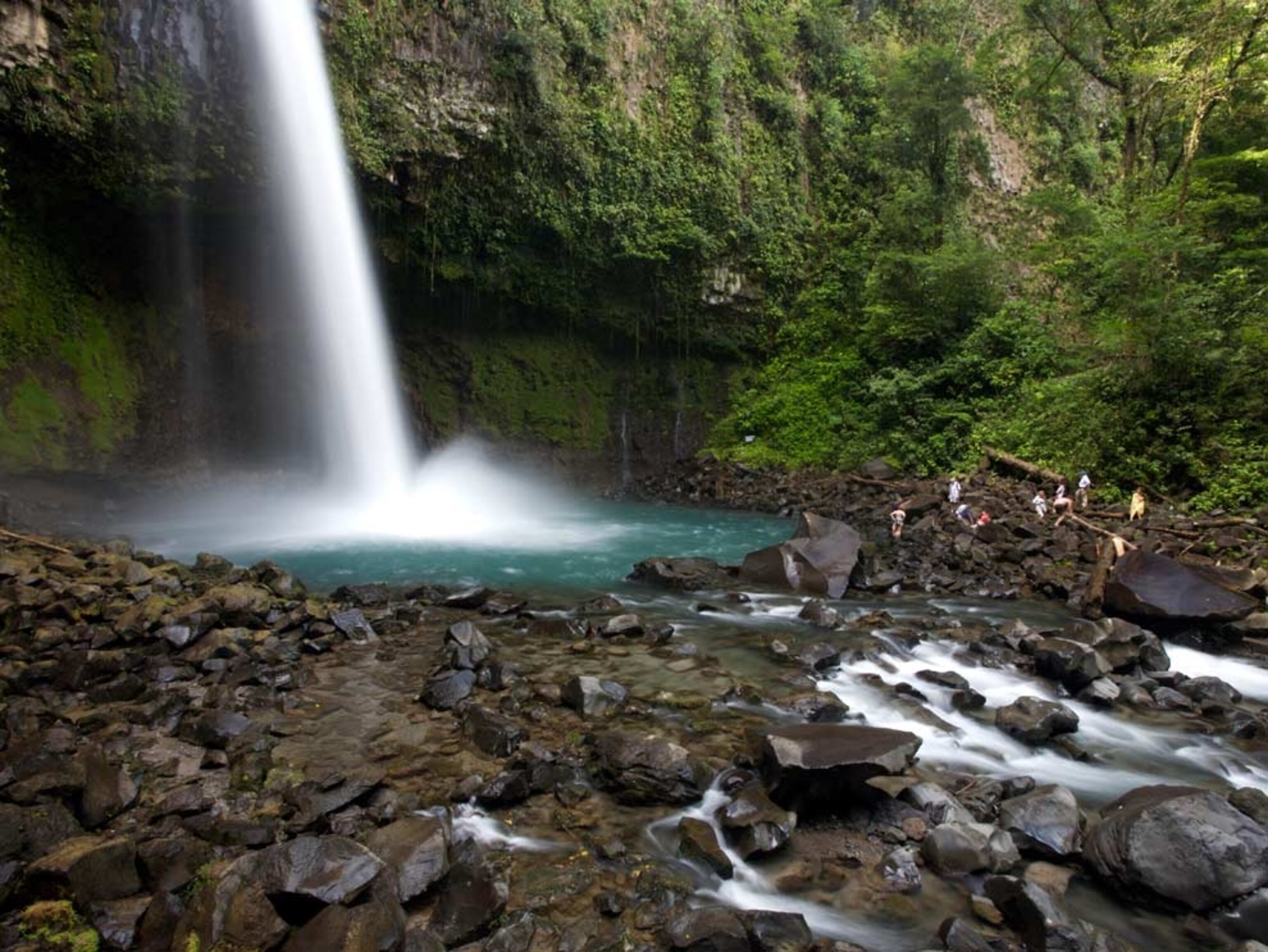 People relaxing on rocks around a misty waterfall