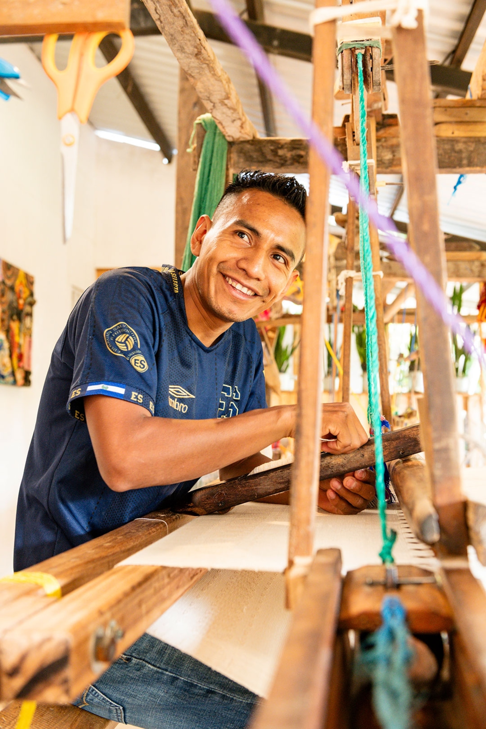 A man smiling as he works his weaving machine in El Salvador.