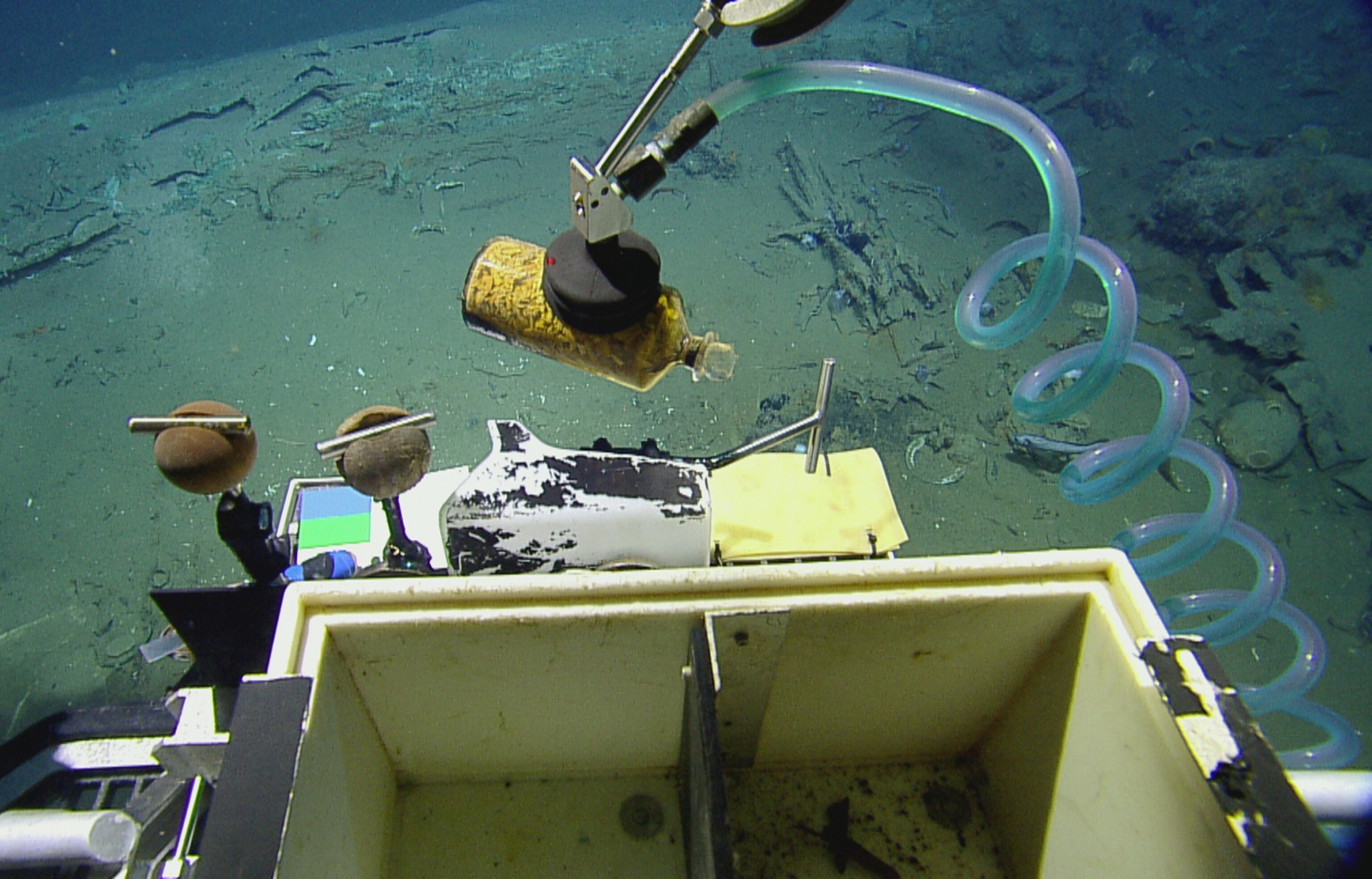 a robotic arm on the remotely operated vehicle picking up a bottle from the seafloor