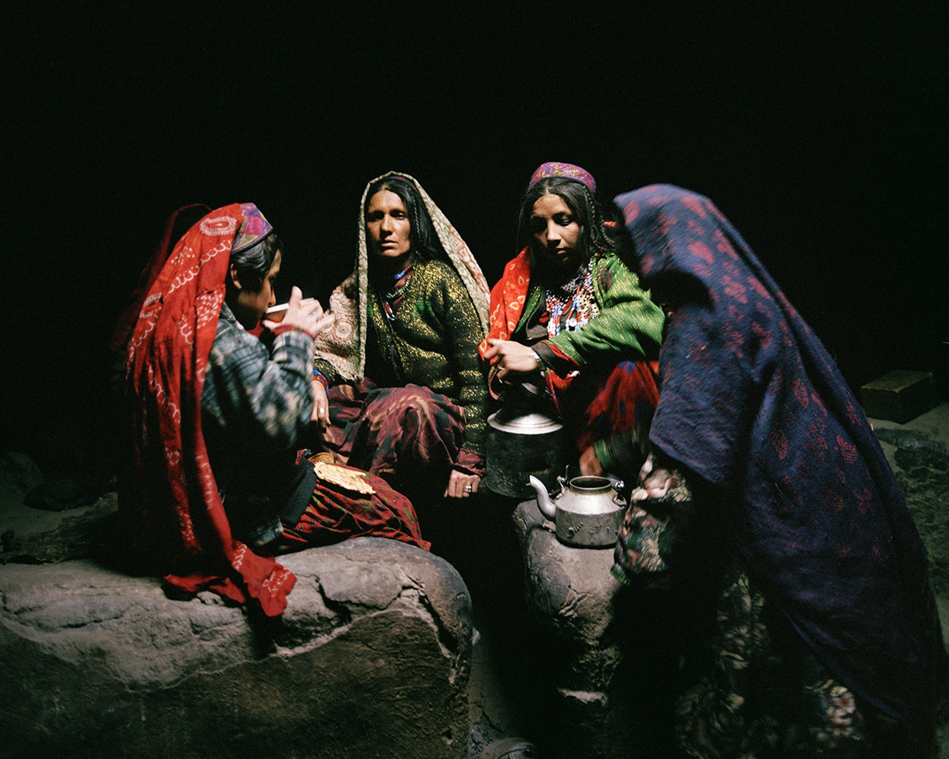Several women and girls sit in a circle drinking out of a bowl.