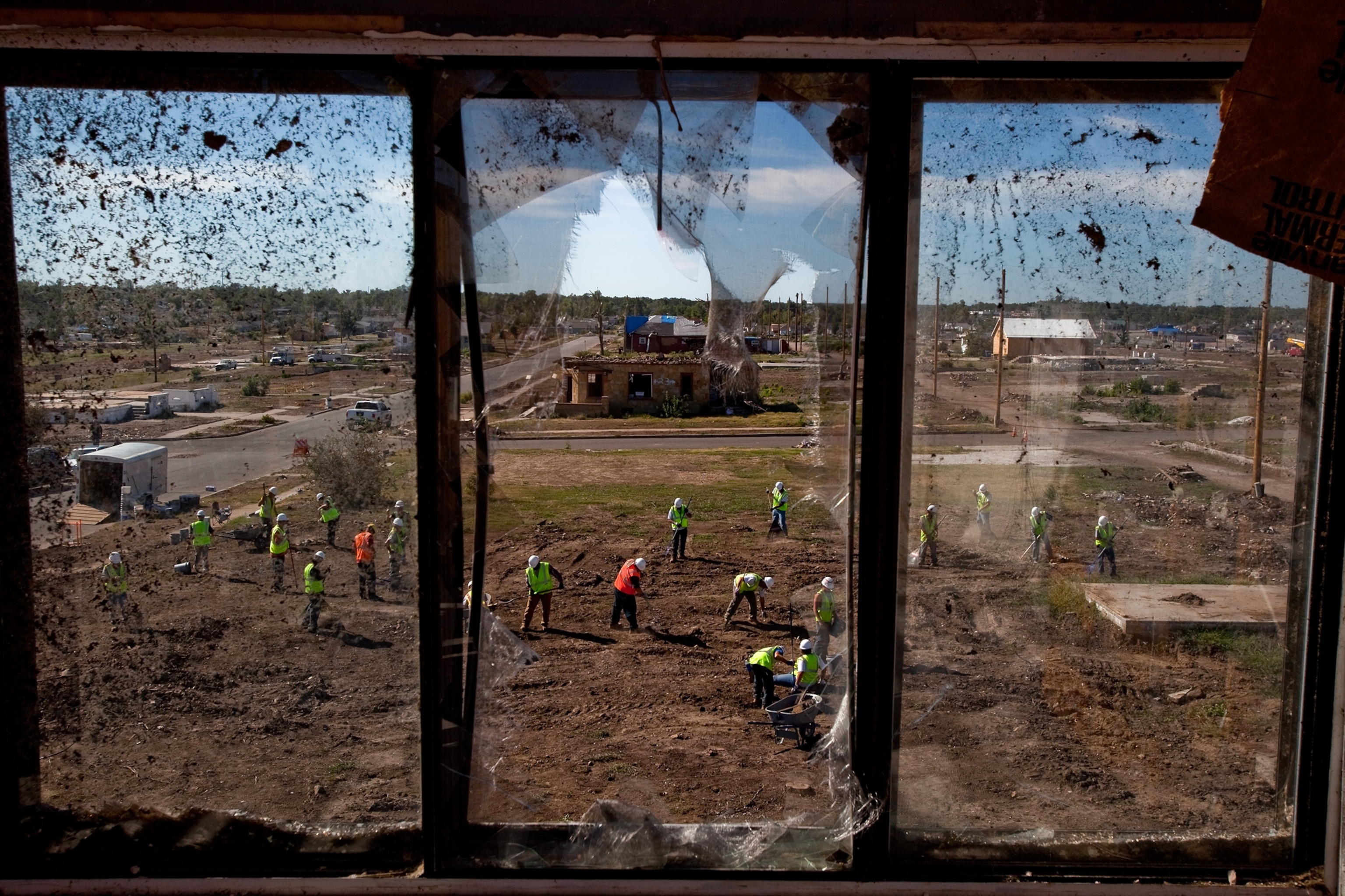 How Joplin Recovered - City workers are seen outside a broken window cleaning up scrap metal and glass shards.
