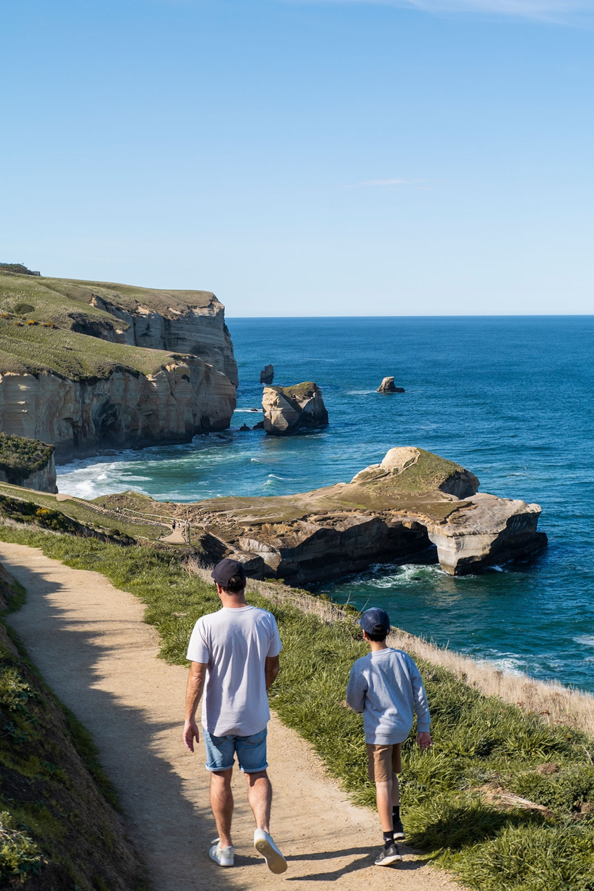 Two people walk the track to Tunnel Beach, Dunedin, New Zealand