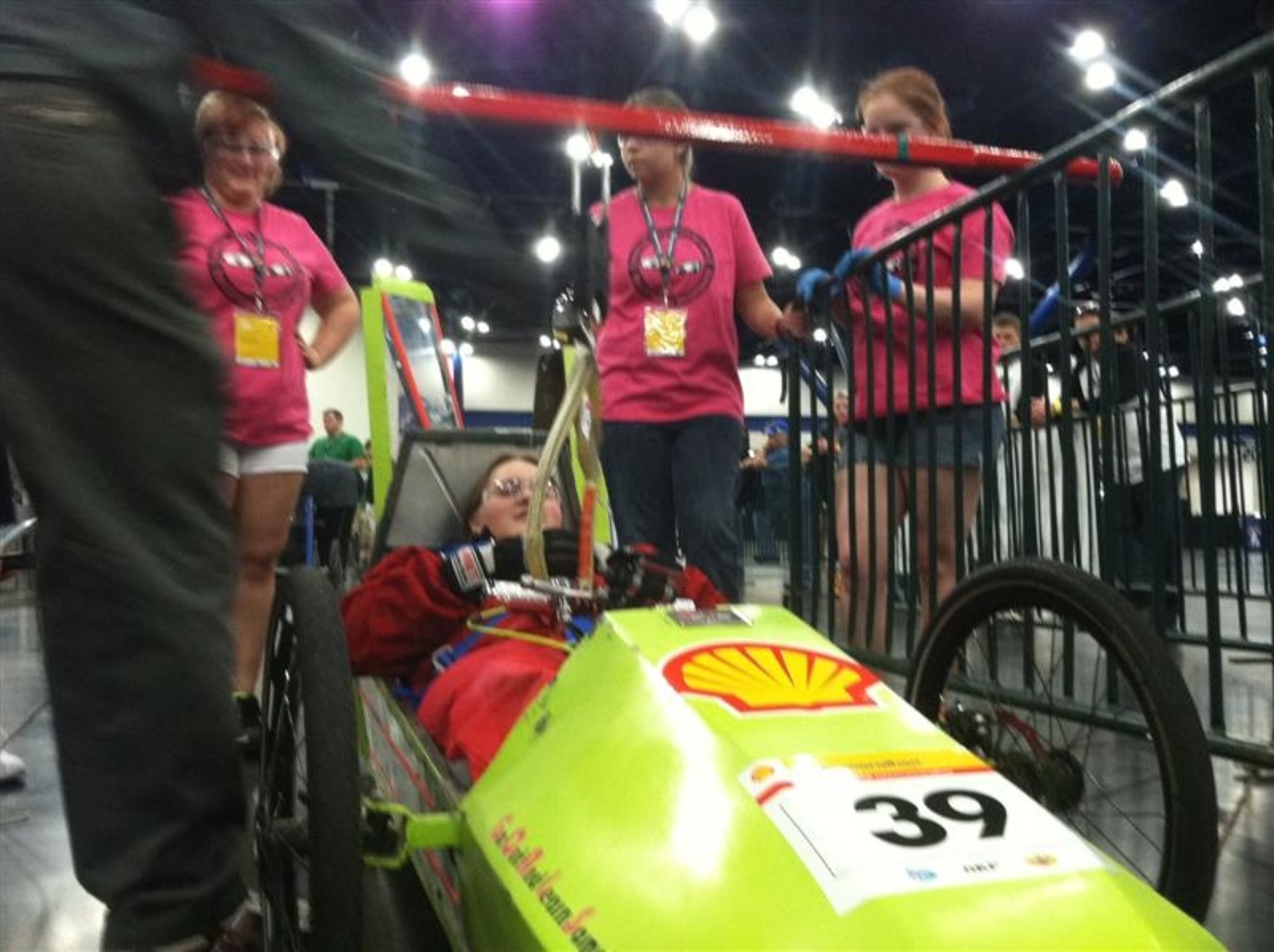 With Dansil Green in the driver's seat, Shell Eco-marathon technical inspectors check the seat belt integrity in the ShopGirls' car, one of a required battery of tests for all competitors. Teammates Kylee Hayter (left), Teagan Fifre, and Samantha Miner-Ball watch. Photo by Marianne Lavelle.