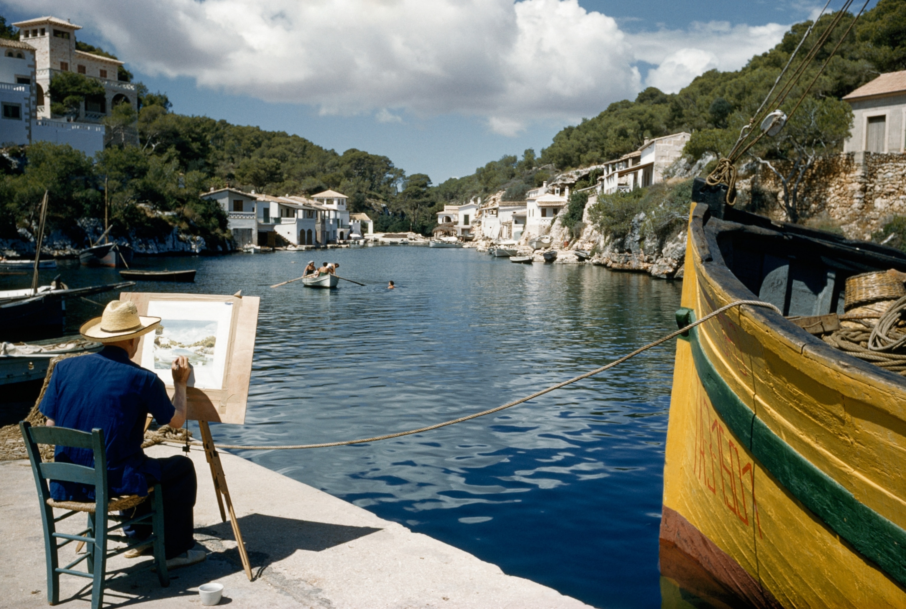 Picture of a man with an easel painting a scene of a harbor on the Spanish island of Majorca