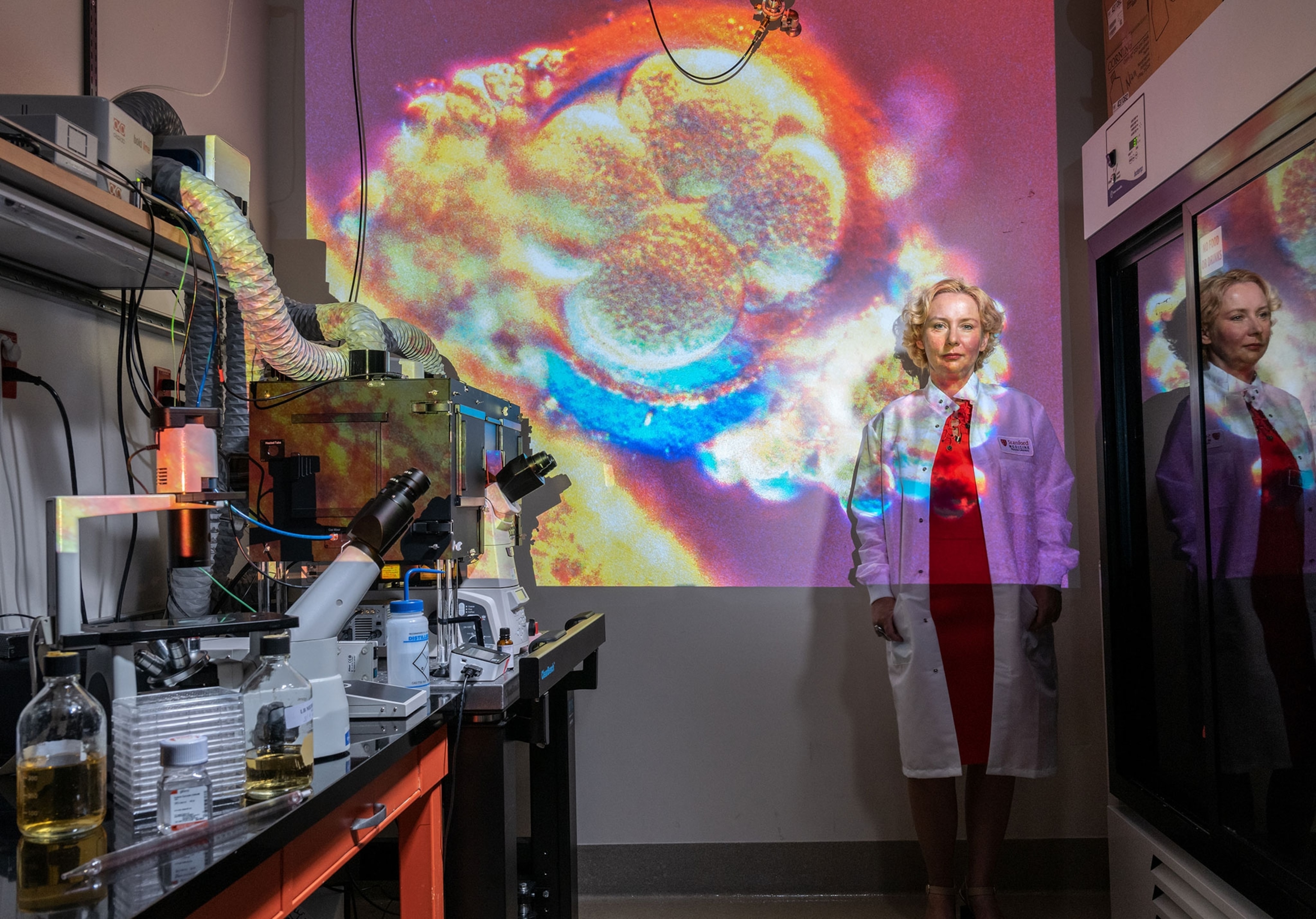 woman in white coat with image of a human embryo projected on her and wall.