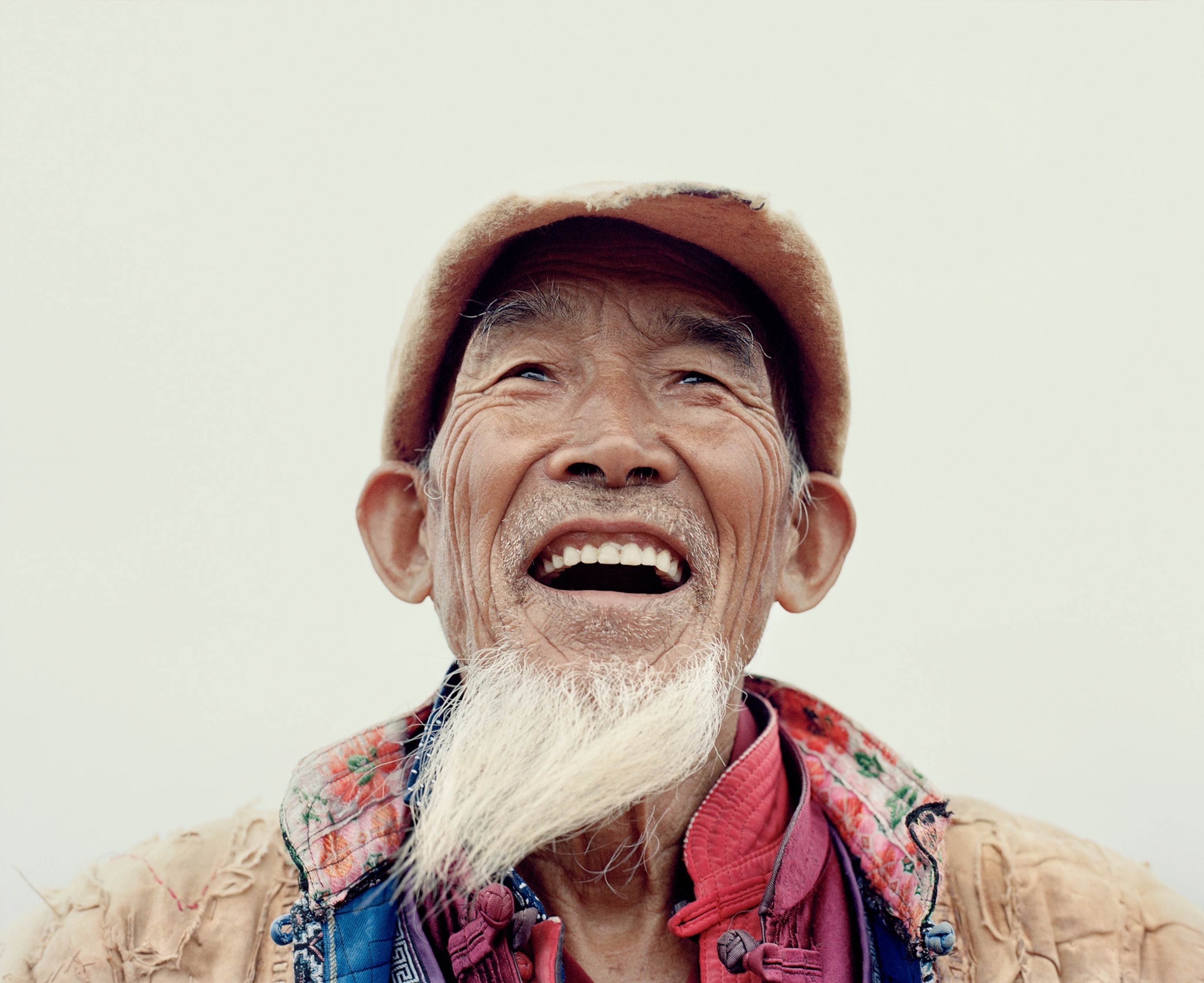 A man with a goatee and a hat smiles with his teeth.