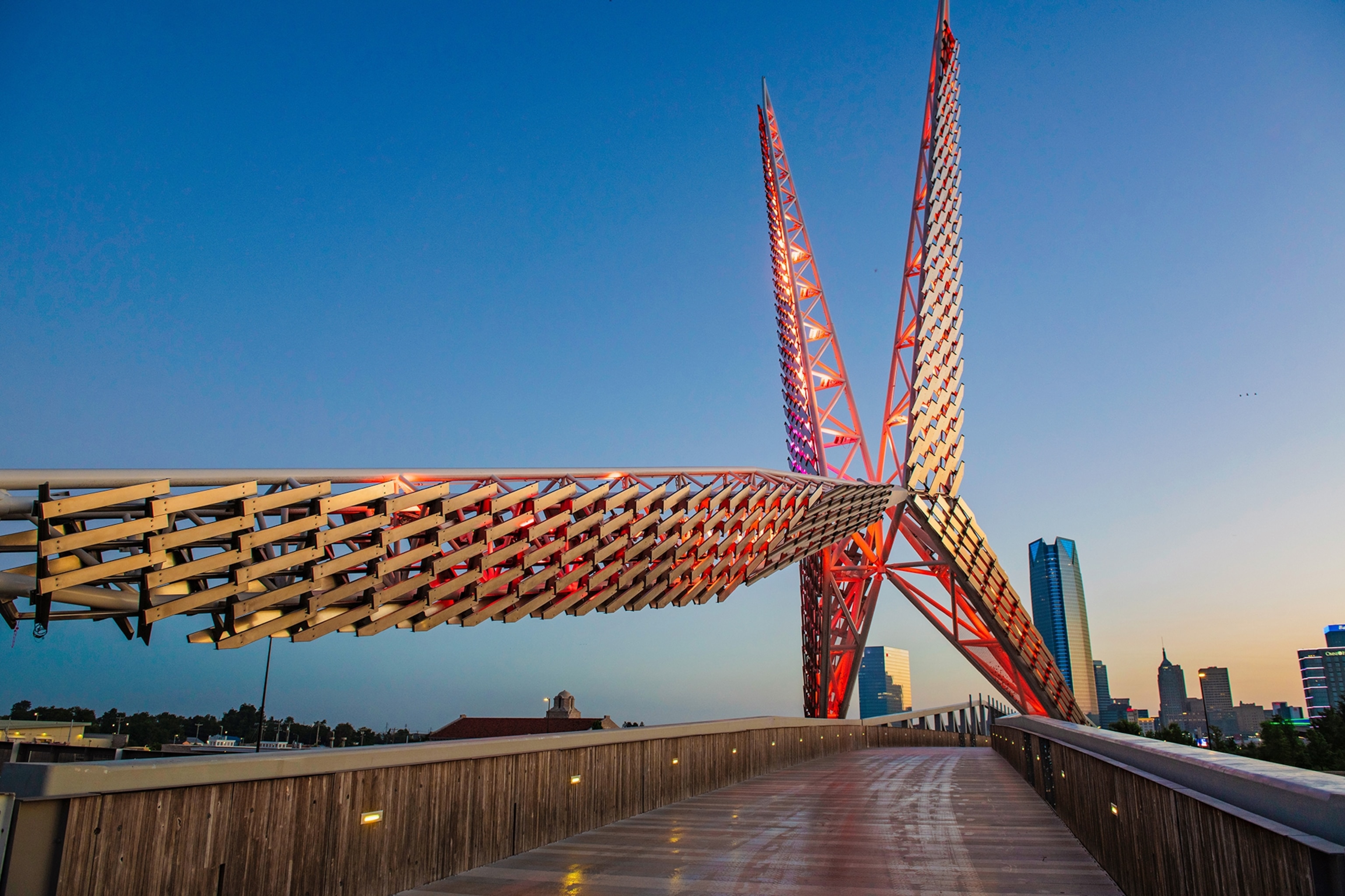 A tall, scissor-shaped construction towers over a bridge in Oklahoma City's Scissortail Park.