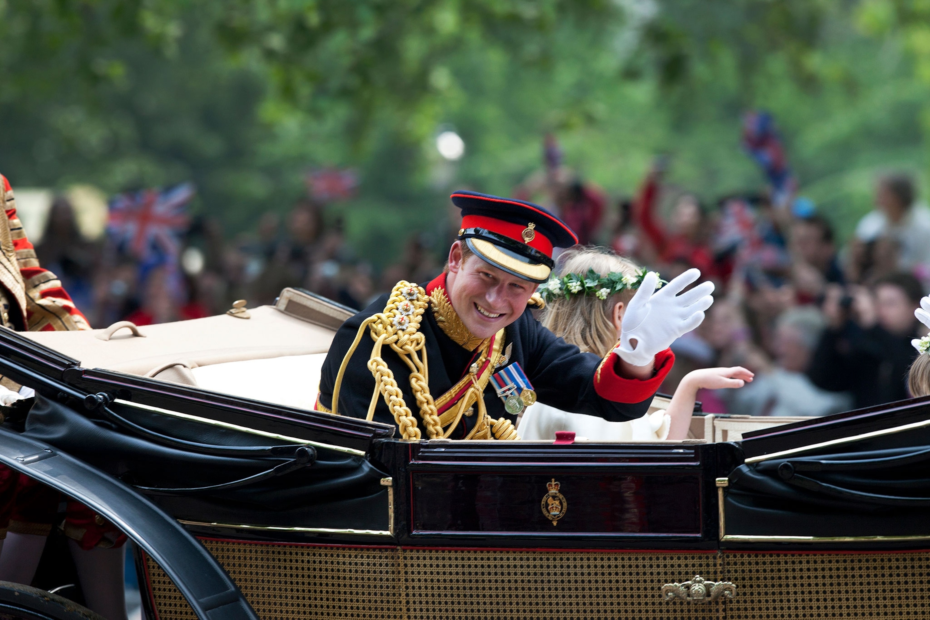 Prince Harry waveing to the crowd by carriage in procession to Buckingham Palace