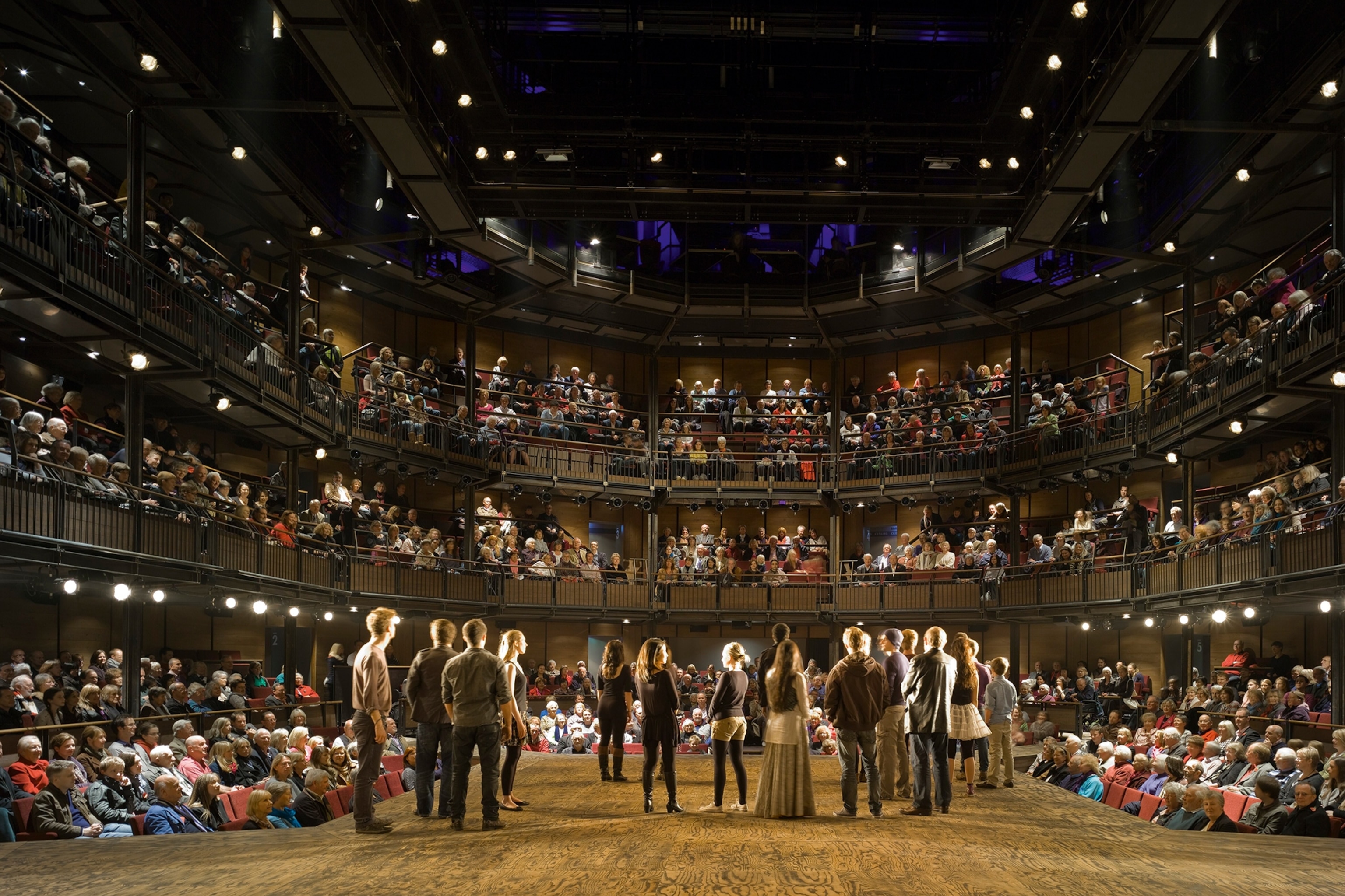 A cast of theatre actors shot from behind, the theatre atrium unfolding in front of them.