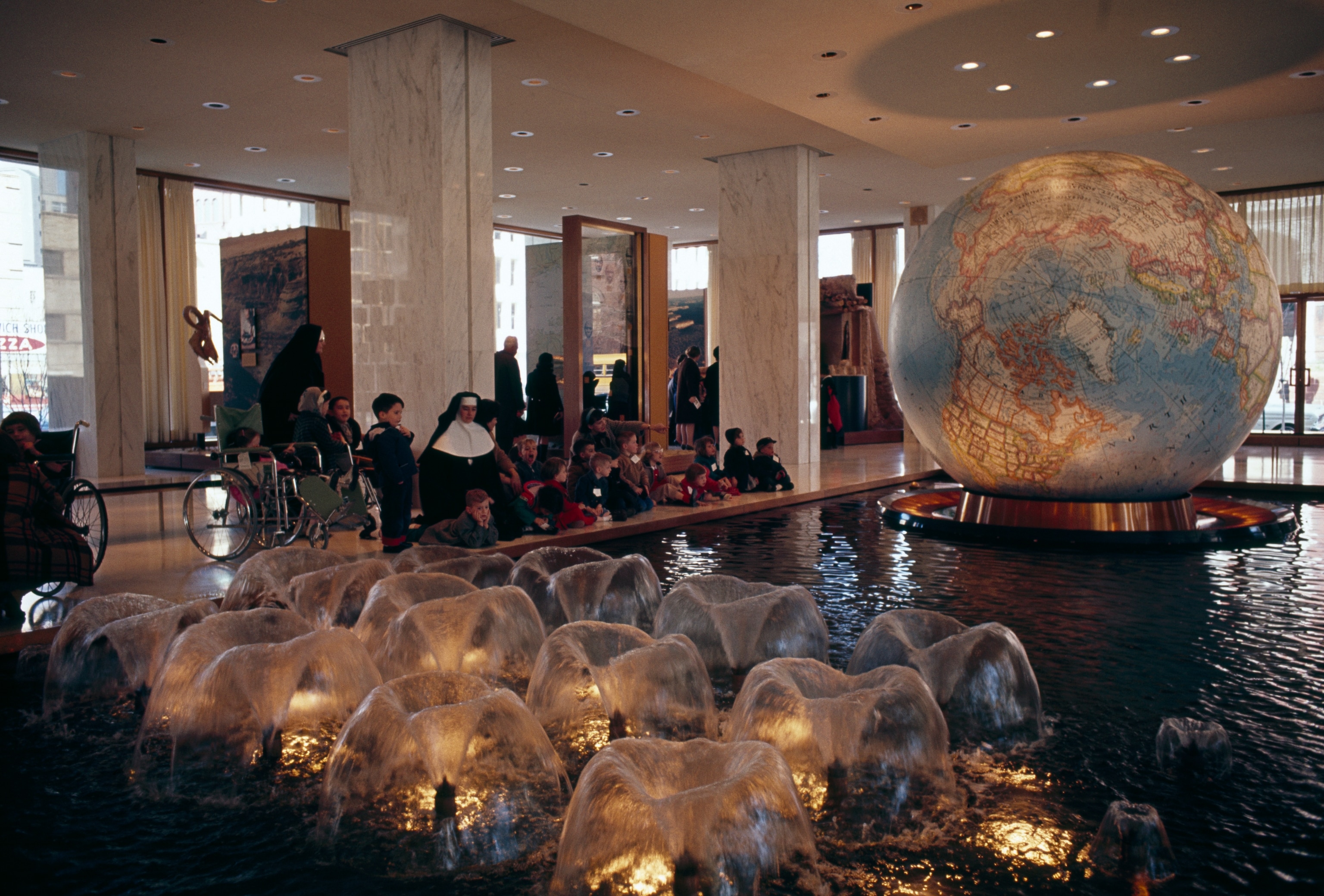 Visitors sit in front of a fountain with a globe