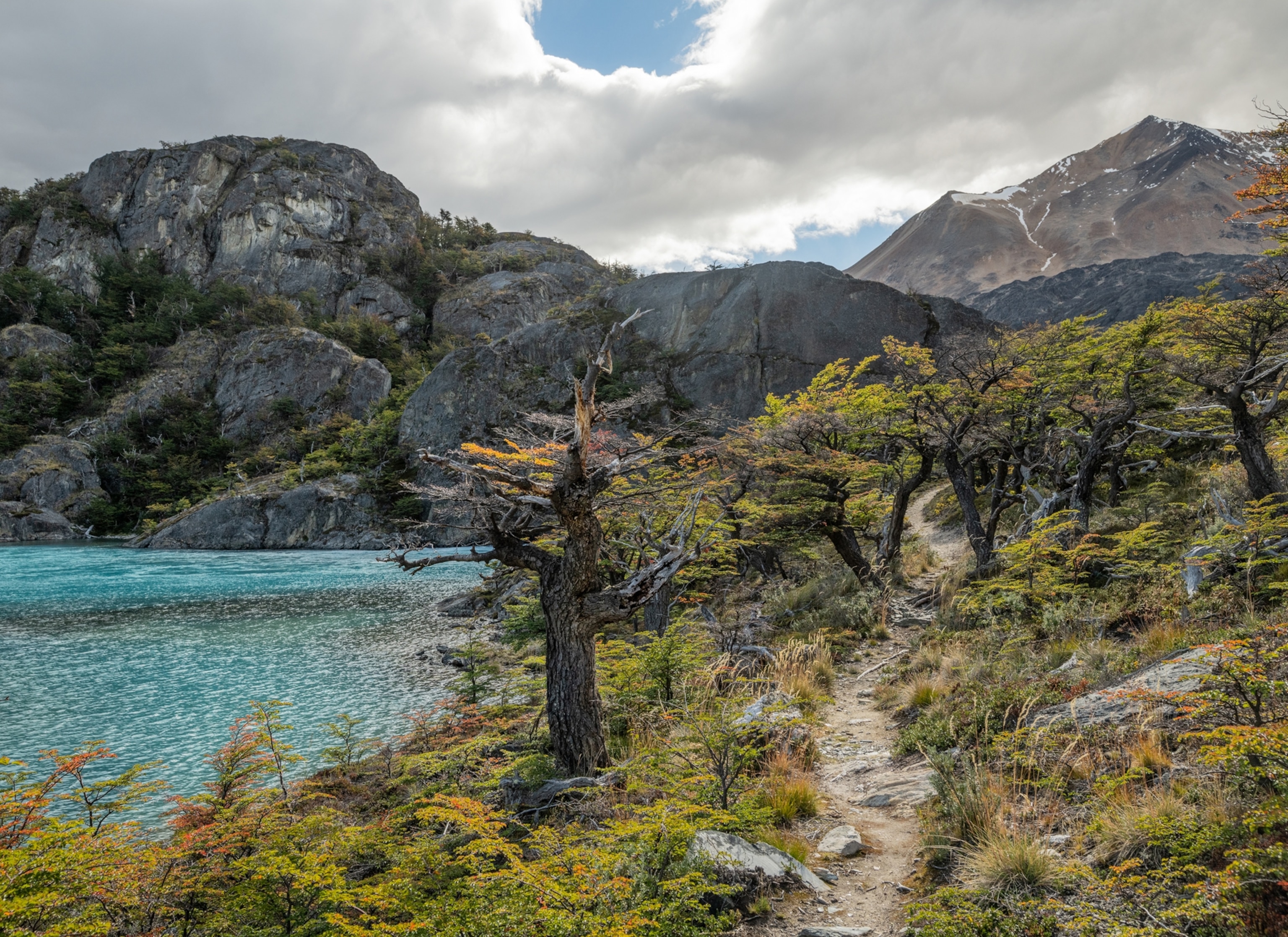 A trail with mountains in the background and a lake to the left.