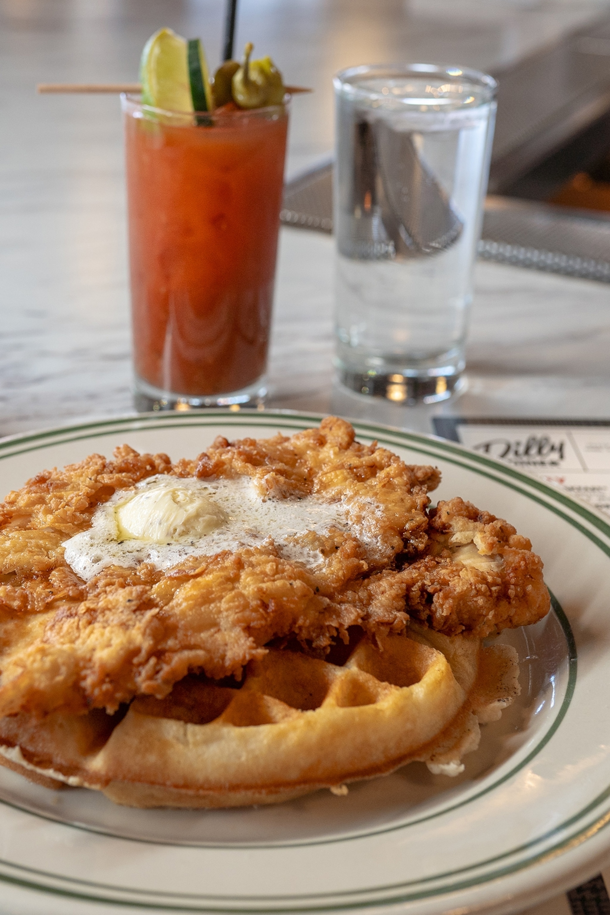 A close-up of a plate of fried chicken on waffles with a side of water and a bloody mary.