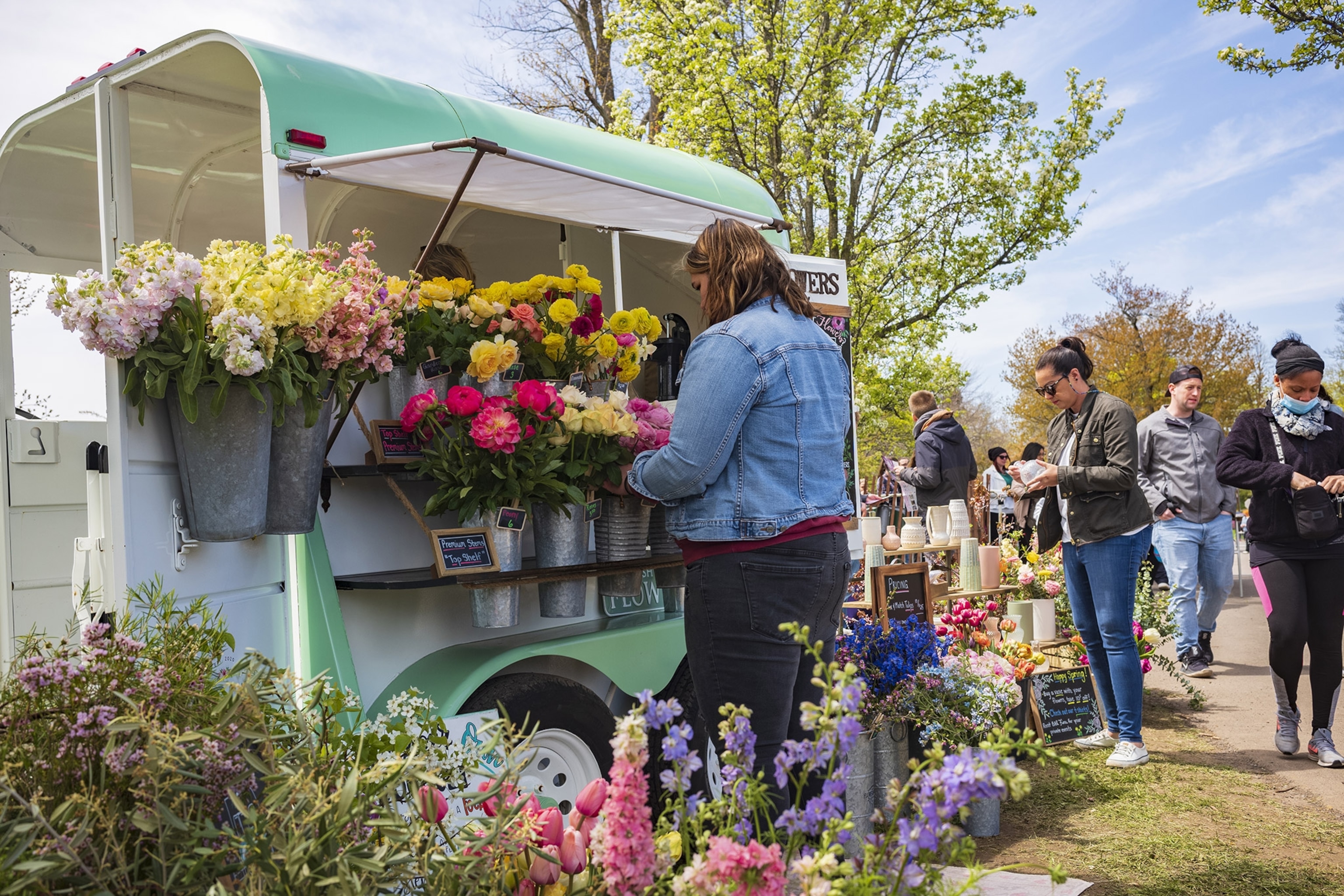 A woman faces a blue cart adorned with flowers with a small crowd of people behind her