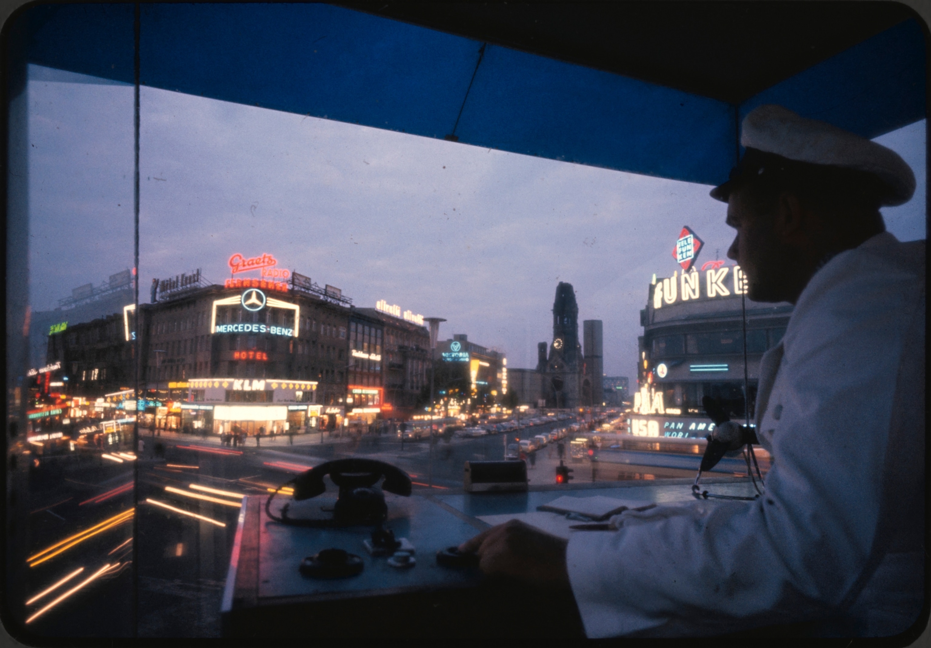 Policeman in a glassed-in observatory pushes buttons to regulate traffic at West Berlin's busiest intersection. Here Kurfürstendamm — Ku'damm to Berliners — begins at the ruined Kaiser Wilhem Memorial Church (opposite) and crosses Joachimstalerstrasse. The Ku'damm, lined with fashionable stores, has become the liveliest shopping artery.