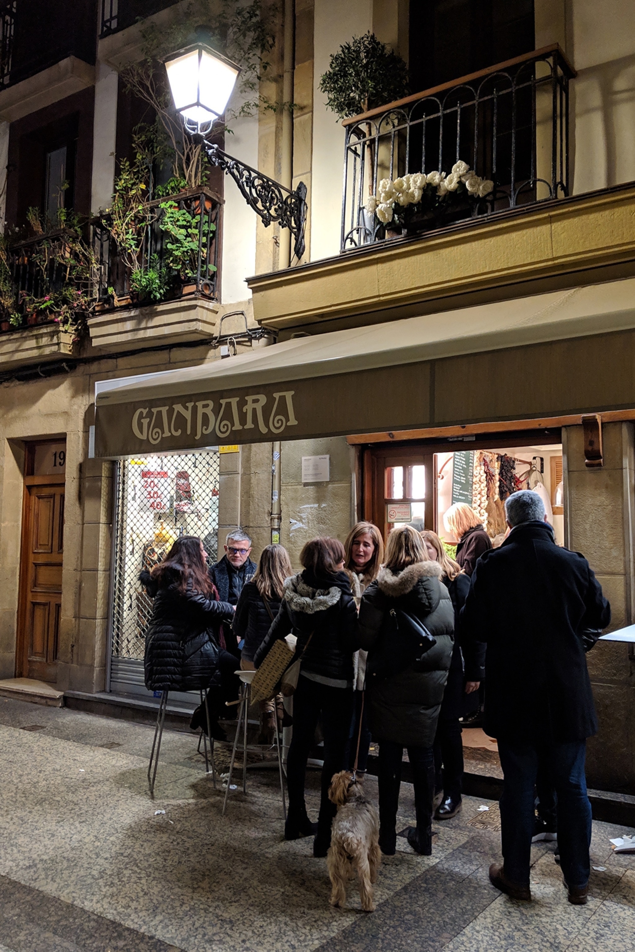 The exterior of a bar with a rustic wooden sign and diners standing in winter coats outside.