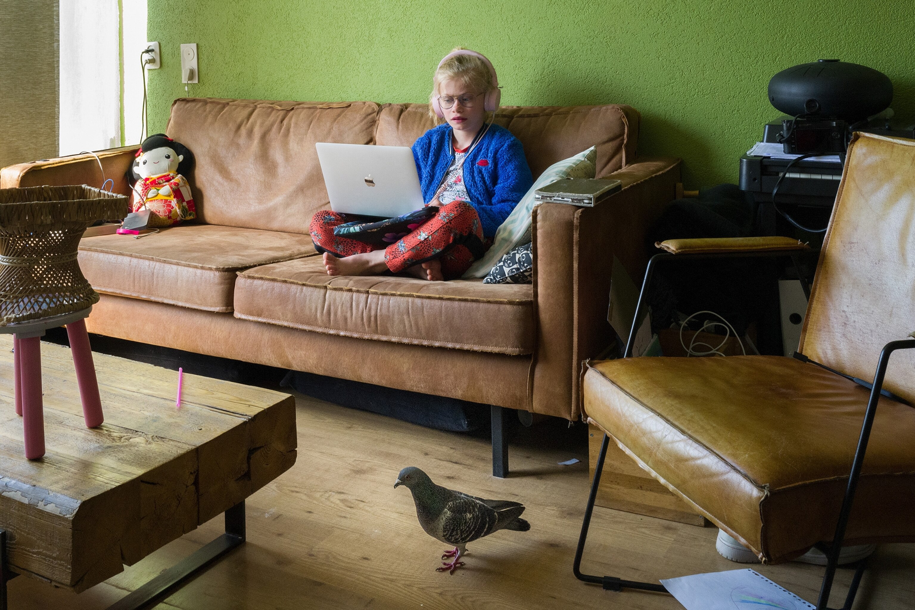 a young girl sitting on the couch and a pigeon walking past her